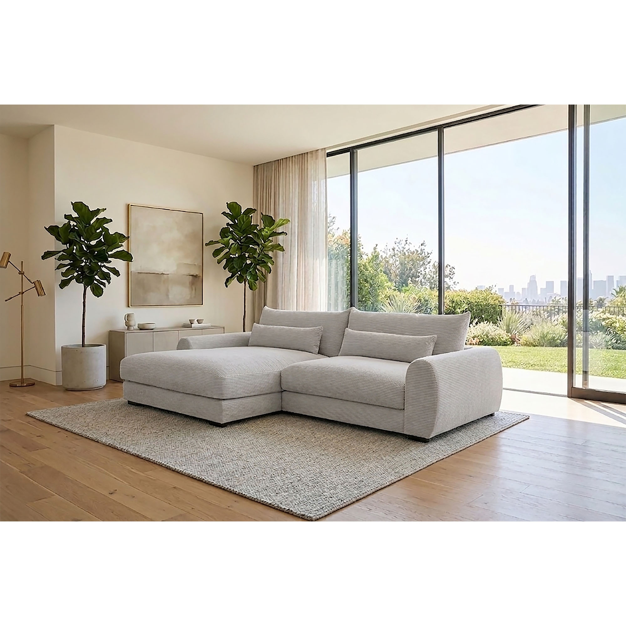 Milieubild eines weißen Ecksofas mit linker Ottomane, breiten Armlehnen und schwarzen Kunststofffüßen in einem hellen Wohnzimmer mit großen Fensterflächen