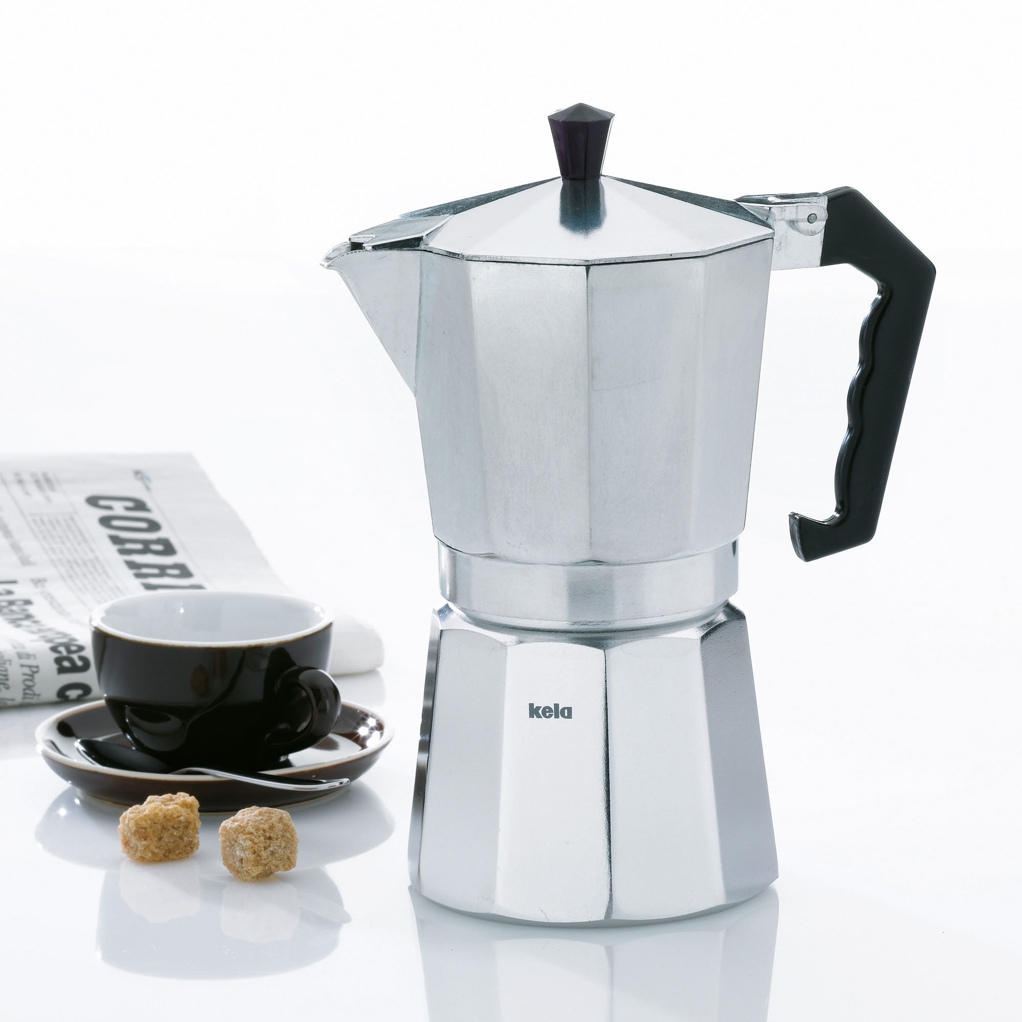 Silberfarbener Espressobereiter auf hellem Untergrund neben kleinen Kaffeetassen und gerösteten Kaffeebohnen