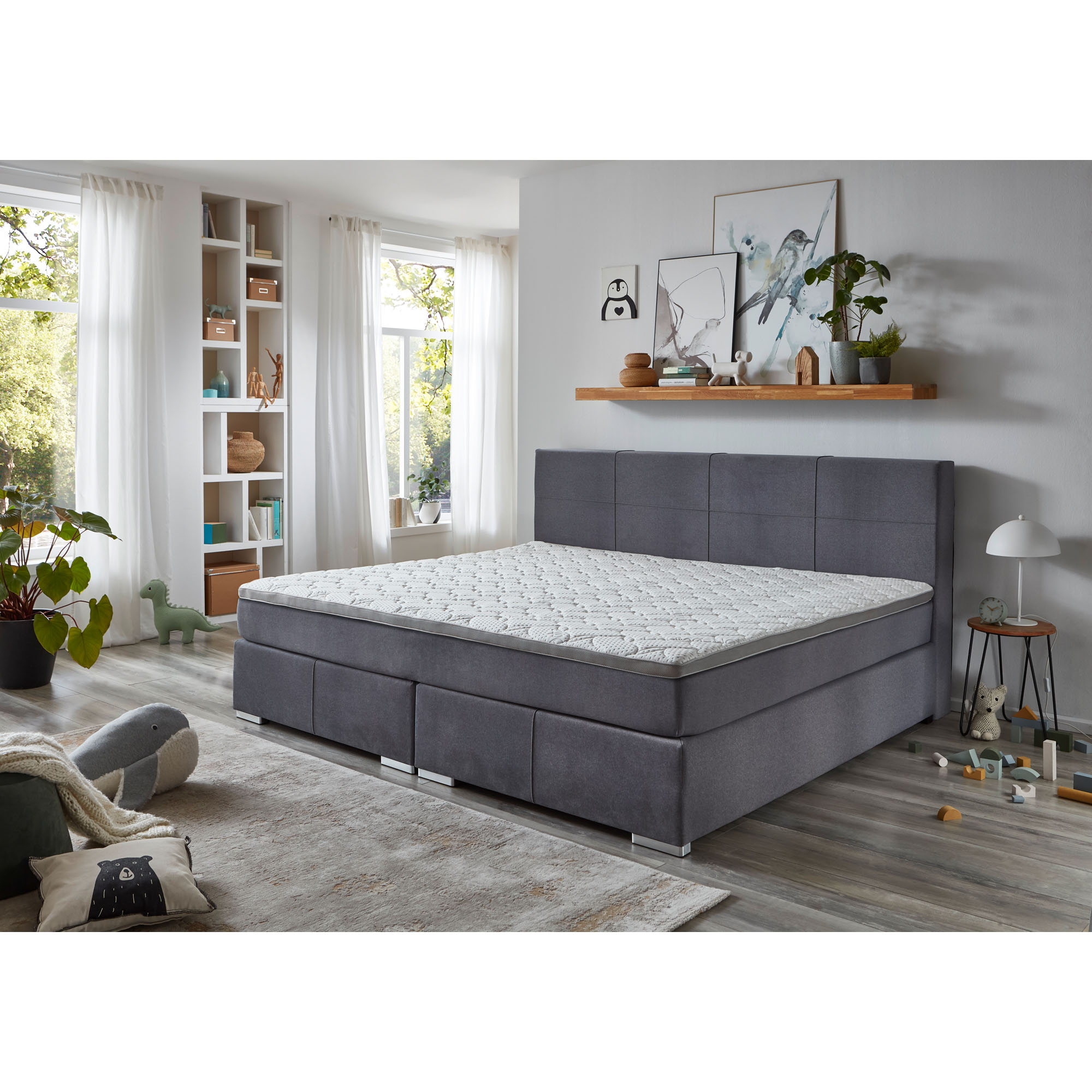 Boxspringbett mit grauem Stoffbezug und Matratze mit Topper in einem hellen Schlafzimmer