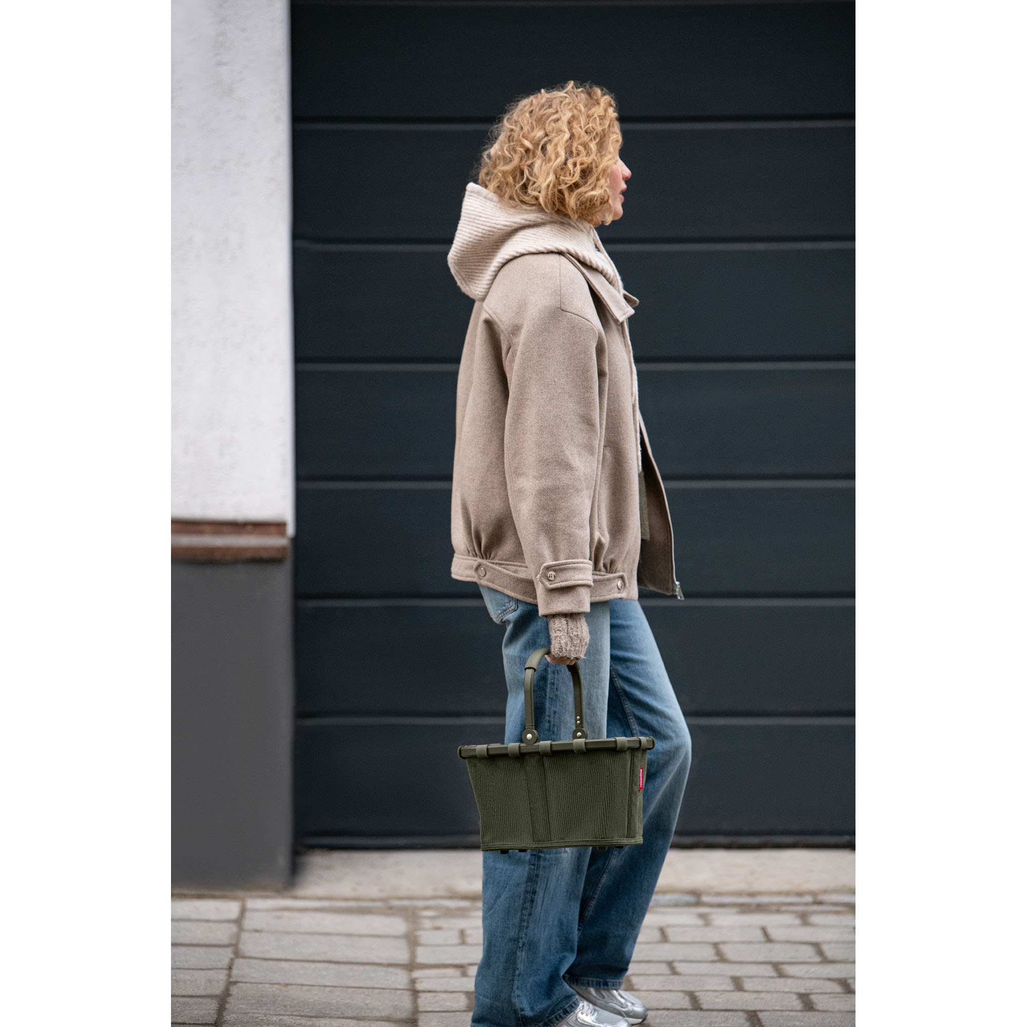 Kleiner Einkaufskorb von Reisenthel, Modell Carrybag XS, in Dunkelgrün aus geripptem Cord, von einer Person am Griff getragen.