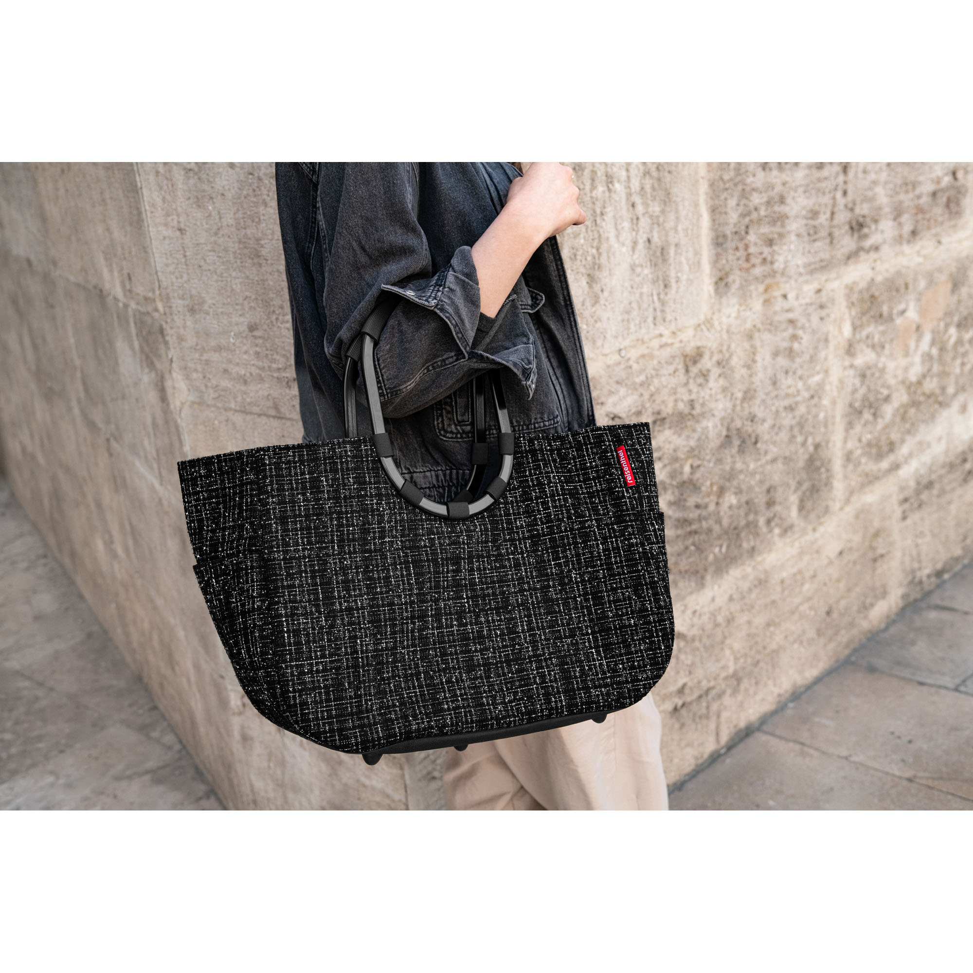 Shopper mit Ringgriffen von Reisenthel, Modell Loopshopper L, in Schwarz mit Bouclé-Struktur, von einer Person an den ovalen Ringgriffen getragen