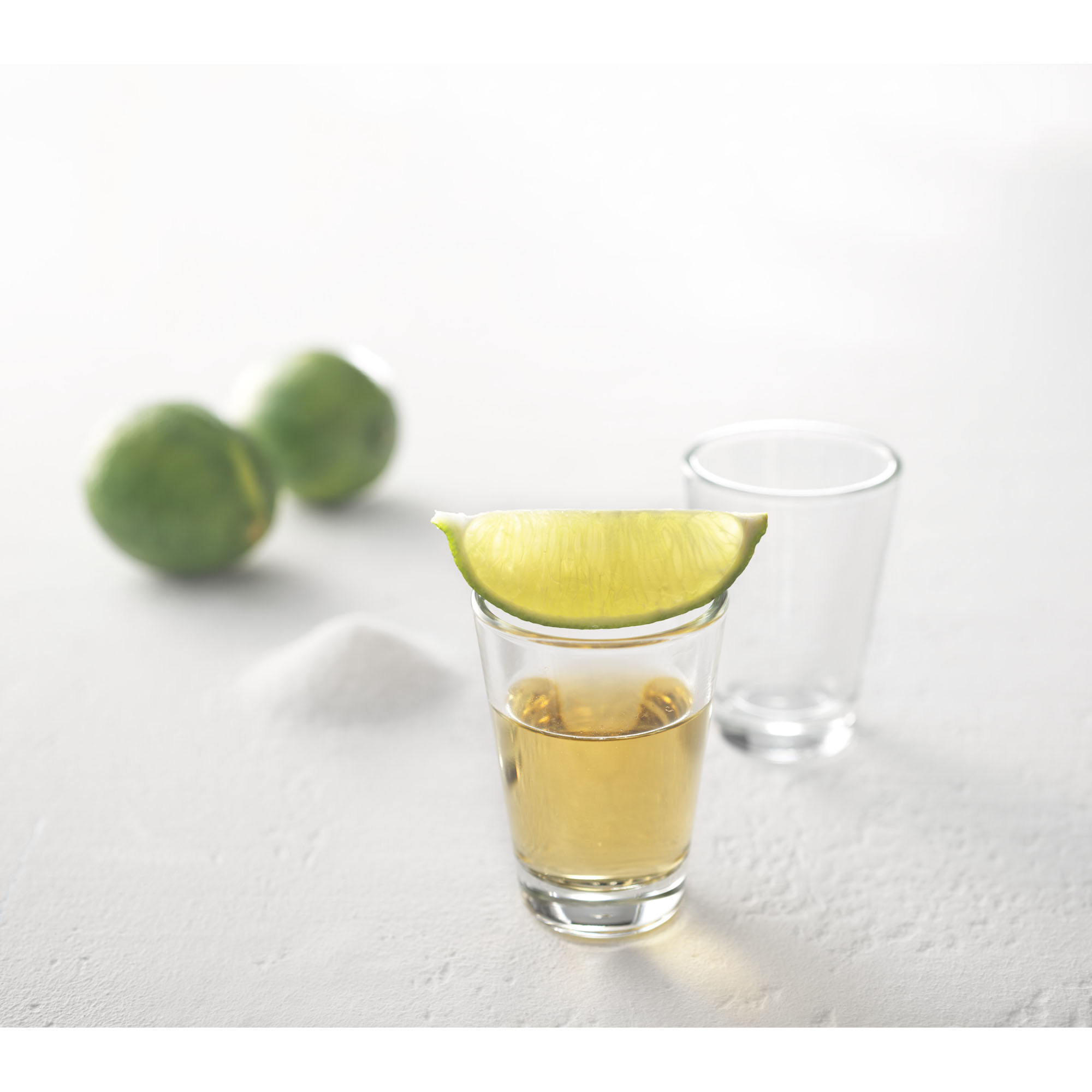 Nahaufnahme eines gefüllten Schnapsglases mit Limettenscheibe auf dem Rand und unscharfem Hintergrund