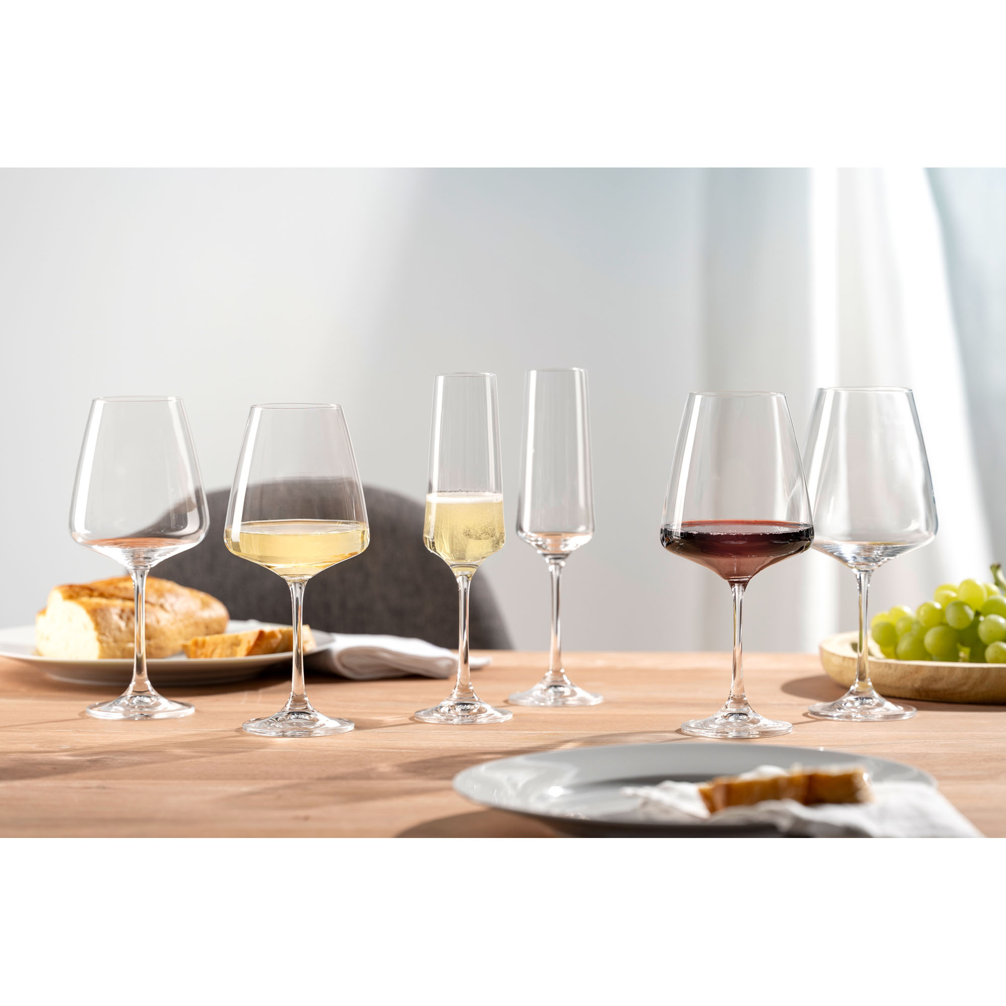 Mehrere Weingläser mit Weißwein Rotwein und Sekt auf einem gedeckten Tisch mit Brot und Trauben