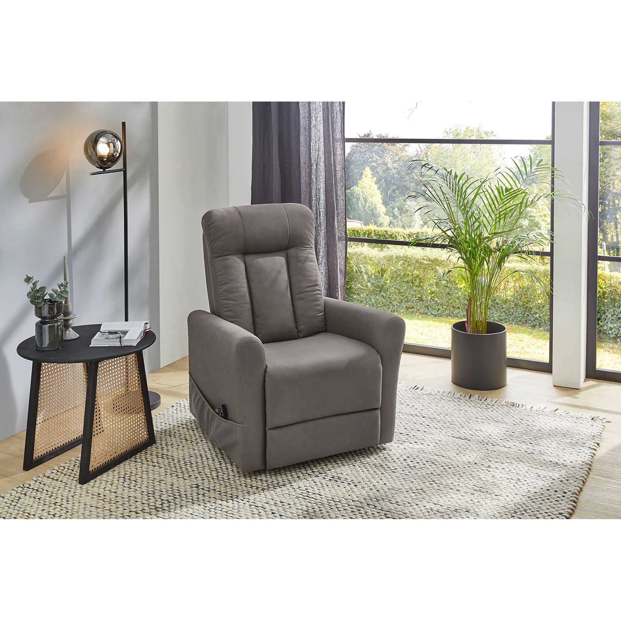 Modernes Wohnzimmer mit Relaxsessel in grauem Stoff, Teppich, Beistelltisch und Pflanze am Fenster.