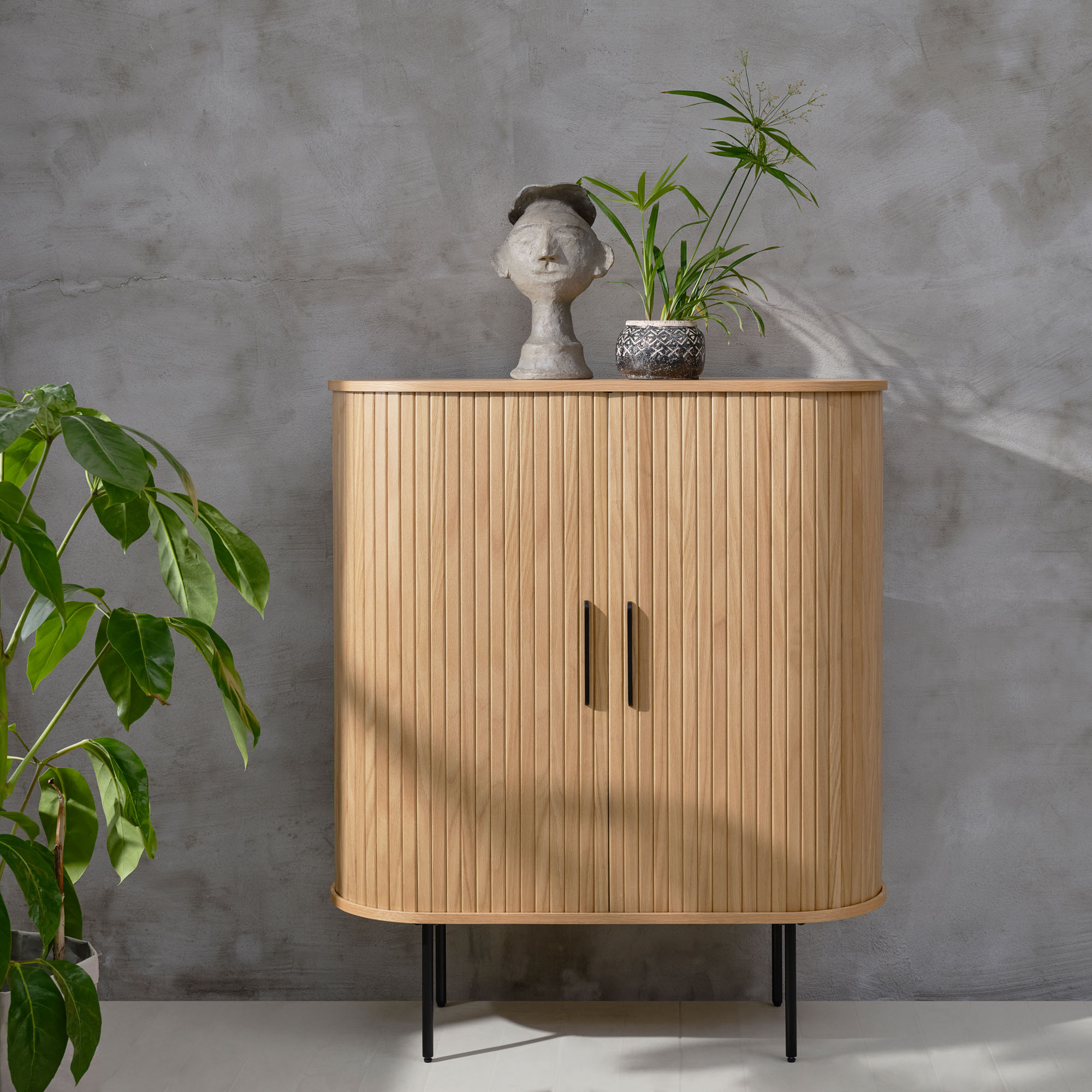 Heller Holzschrank mit Lamellenfront, dekoriert mit Pflanze und Skulptur im Wohnraum