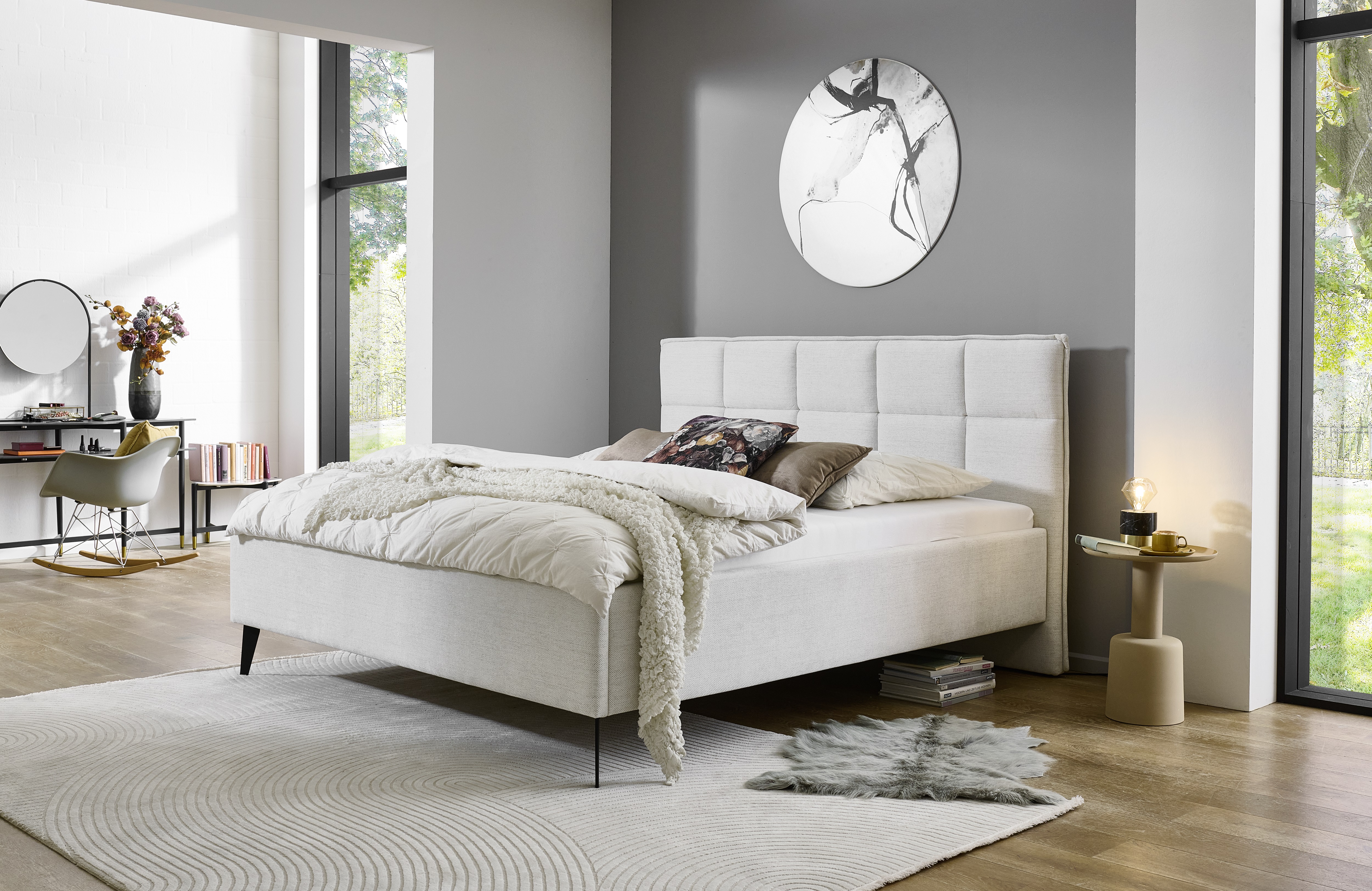 Helles Polsterbett mit gestepptem Kopfteil in modernem Schlafzimmer mit grauer Wand, großem Fenster und stilvoller Einrichtung