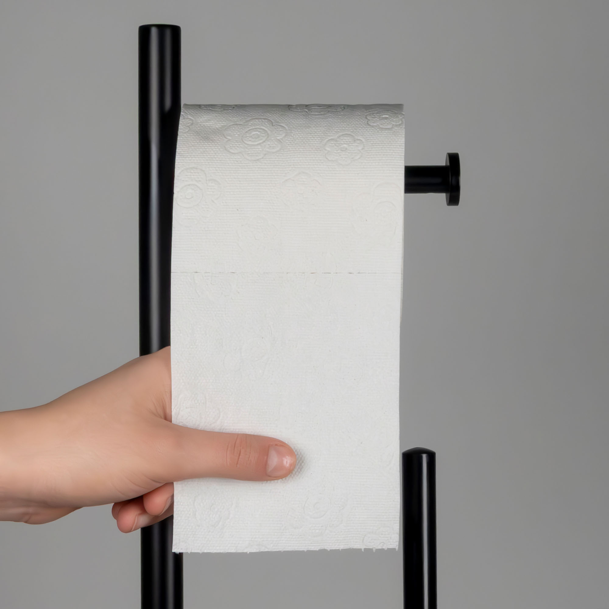 Nahaufnahme einer Hand beim Abrollen von weißem Toilettenpapier am schwarzen seitlichen Haltearm der Toilettengarnitur