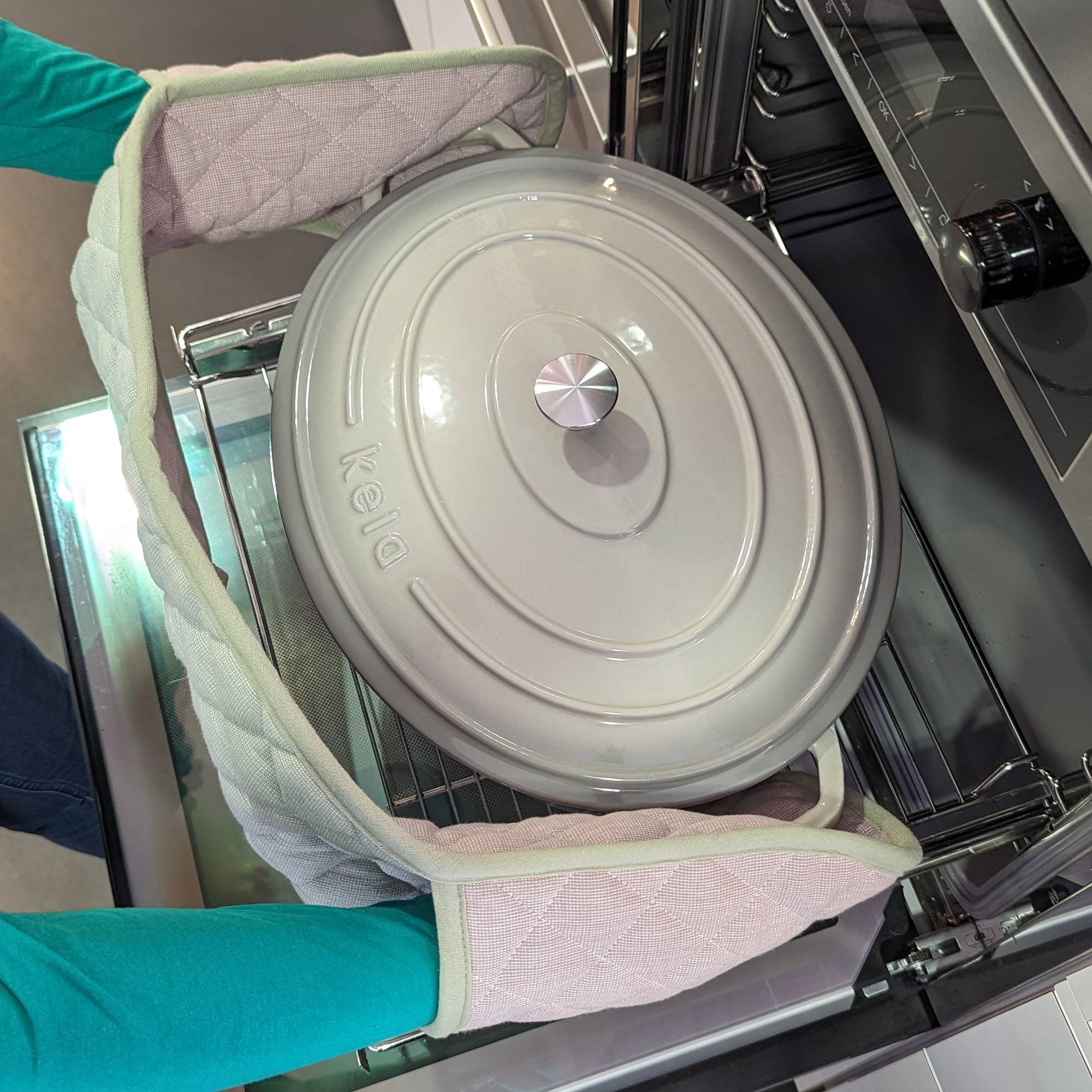 Eine Person nimmt einen Bräter mit Deckel mithilfe des doppelten Ofenhandschuhs aus dem geöffneten Backofen