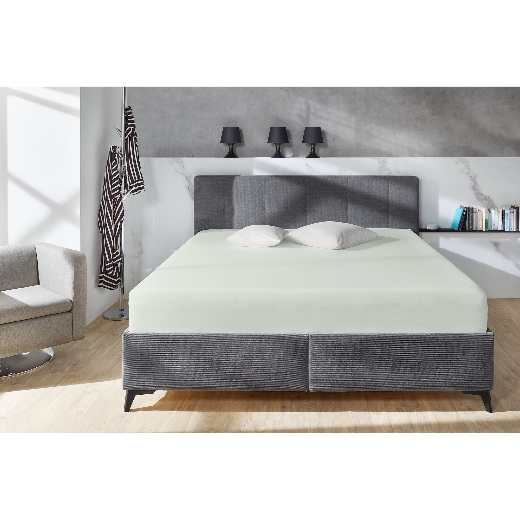 Boxspring-Spannbetttuch in Hellgrau auf einem grauen Boxspringbett in einem Schlafzimmer; zwei helle Kissen liegen am Kopfende; Größe 100 x 200 x 38 cm.
