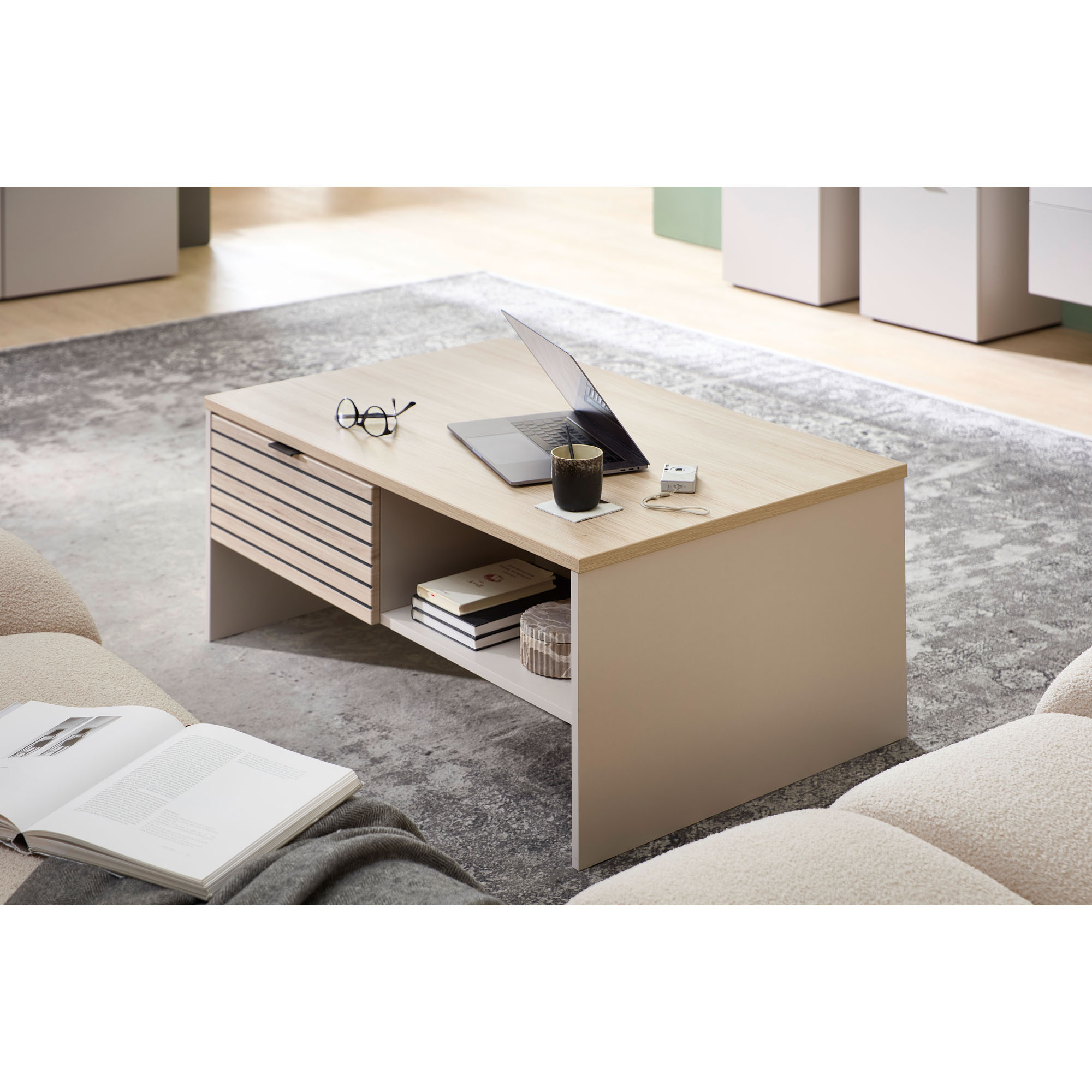 Couchtisch aus hellem Holz in einem Wohnzimmer, dekoriert mit Laptop, Getränk und Brille; im Hintergrund Sofa, Teppich und weitere Möbel sichtbar.