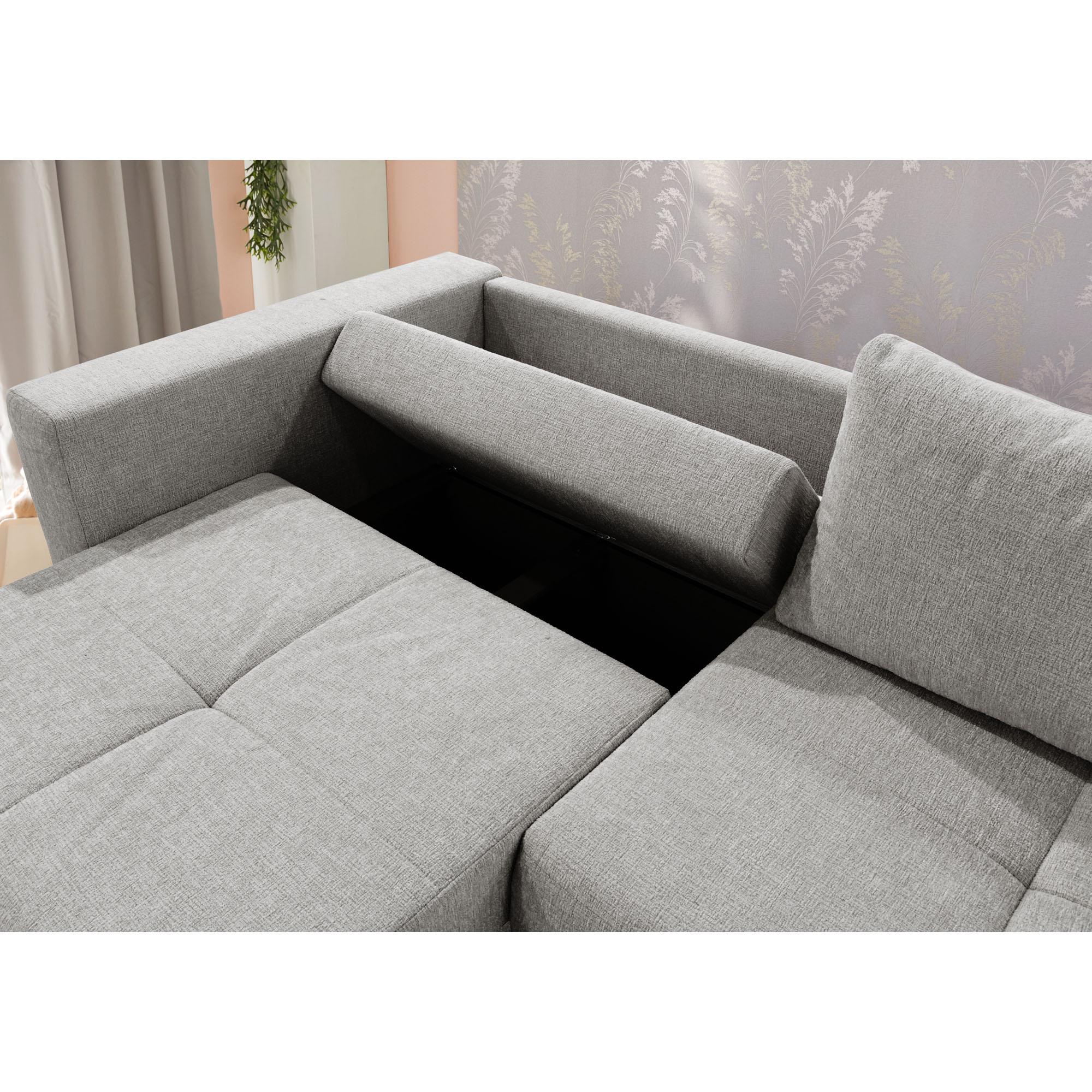 Graues Schlafsofa mit aufgeklapptem Bettkasten und sichtbarem Stauraum für Decken und Kissen