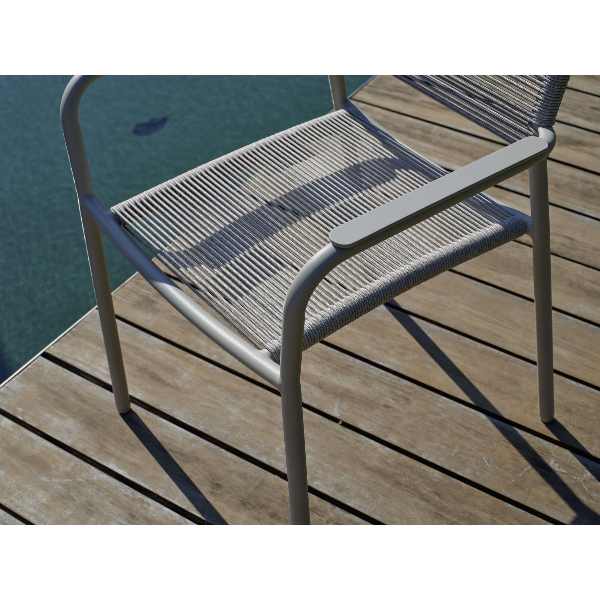 Geflochtene Sitzfläche eines Gartenstuhls auf Holzdeck neben Wasserfläche