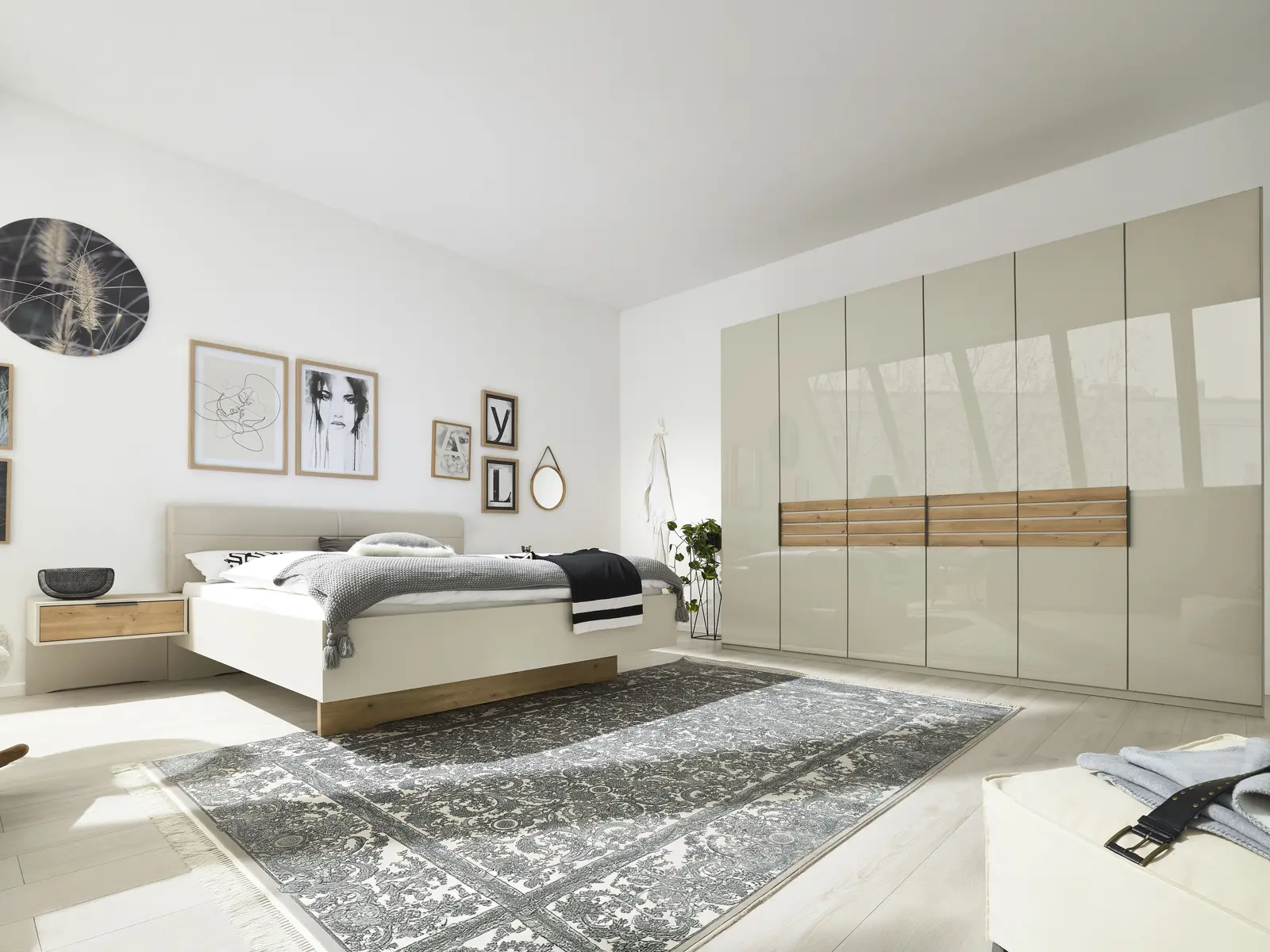 Helles Schlafzimmer mit Doppelbett, Wandbildern und großem Drehtürenschrank in Beige mit durchgehendem Holzakzent in der Mitte