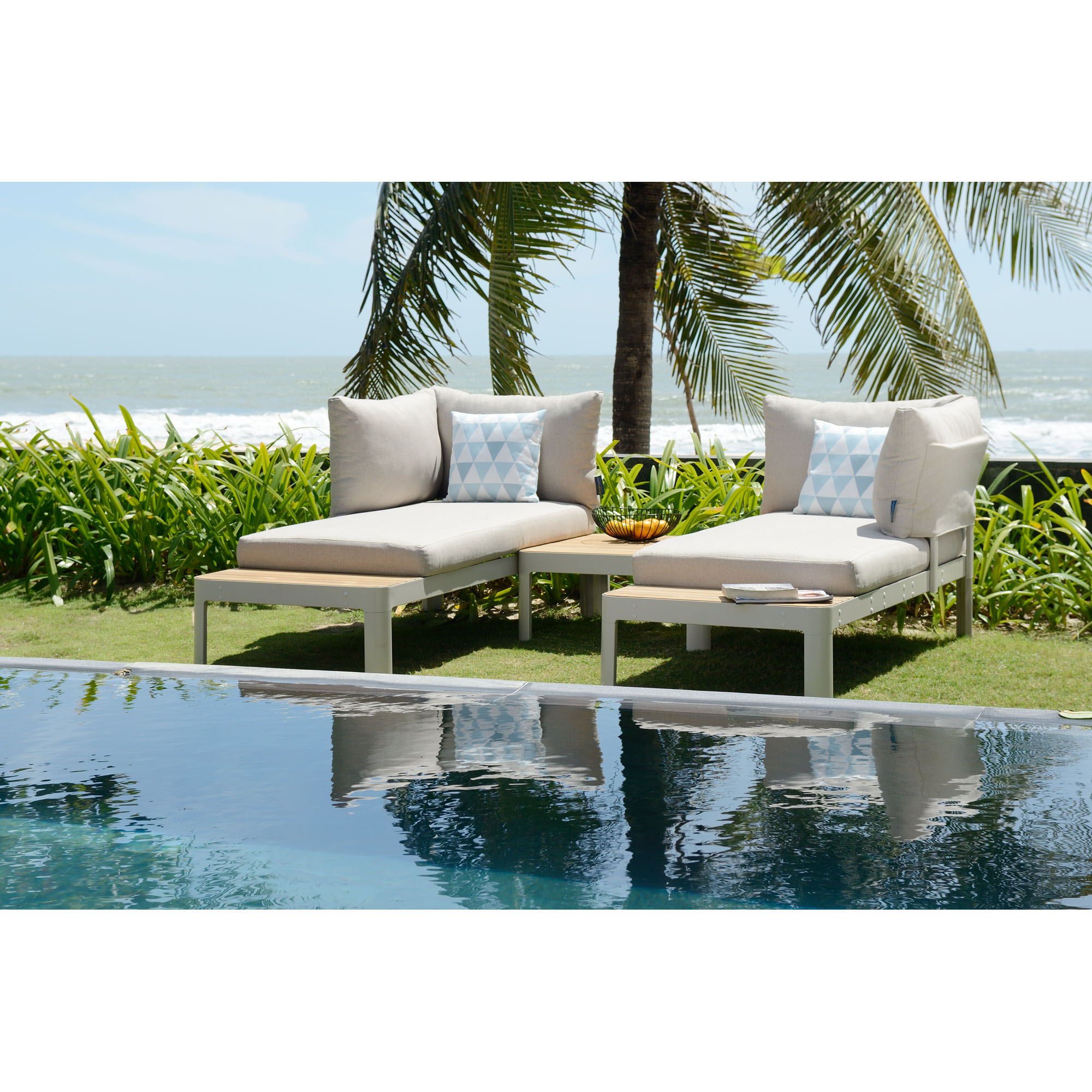 Garten Loungegruppe mit zwei Sofa Elementen und Ablage auf einer Rasenfläche am Pool mit Palmen im Hintergrund