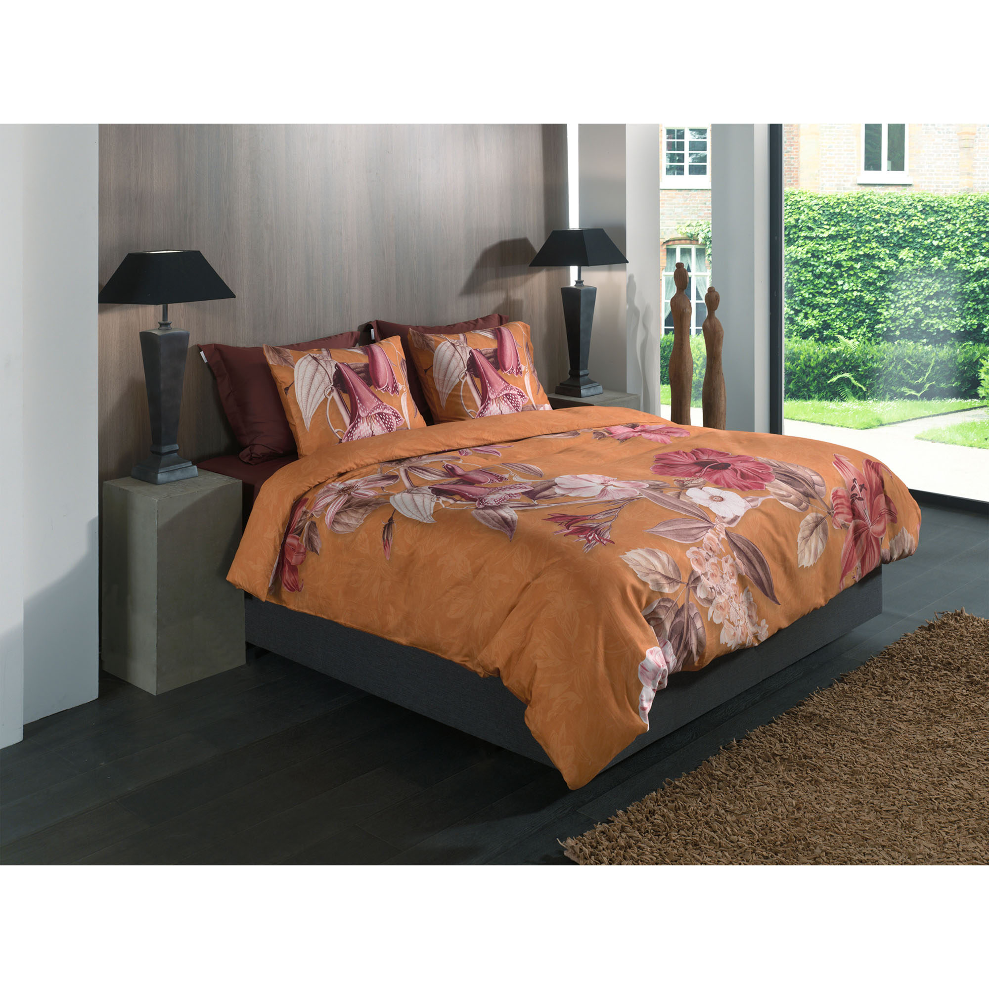 Bettwäsche Malu in Orange, 135 x 200 cm: bezogenes Bett in seitlicher Schlafzimmerszene mit orangefarbenem Grund und großen rosa Blüten.