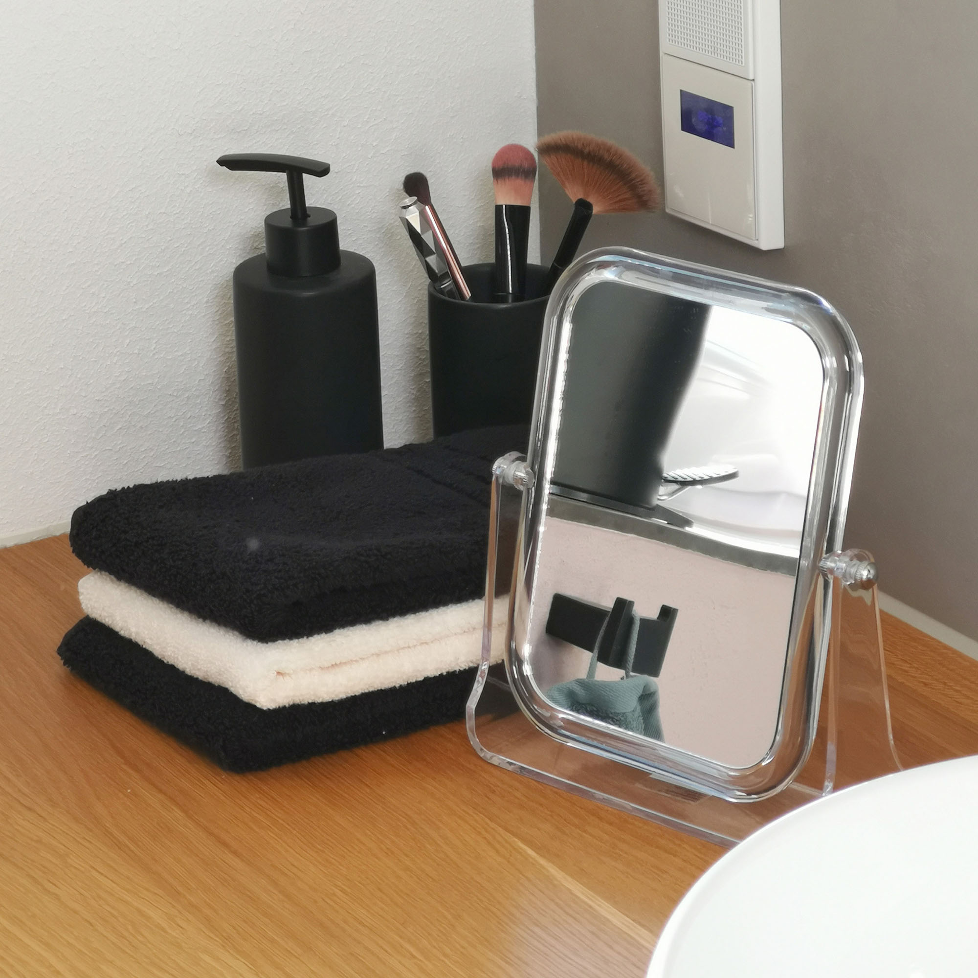 Rechteckiger Kosmetikspiegel mit Standfuß auf einer Holzablage neben Badaccessoires