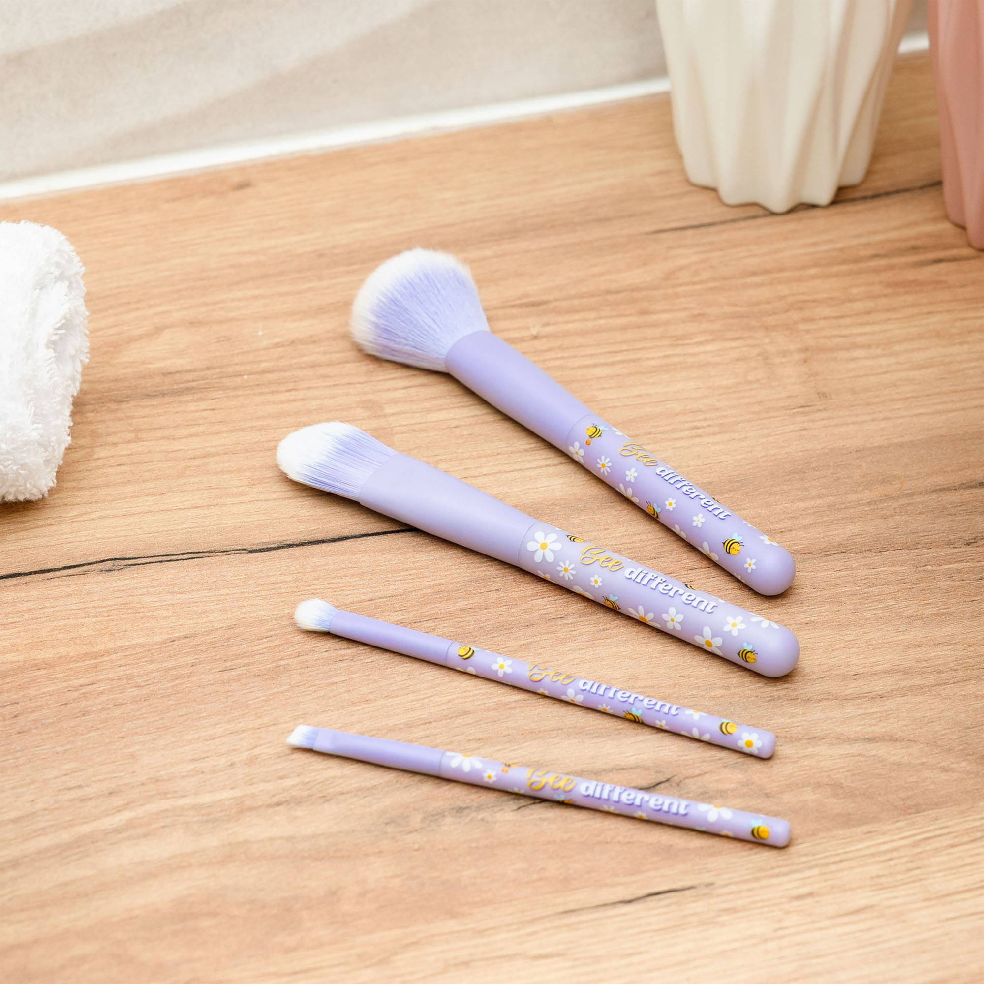 Vier lilafarbene Make-up-Pinsel im Bienen-Design, mit vier Pinseln auf einer hellen Holzfläche ausgelegt gezeigt.