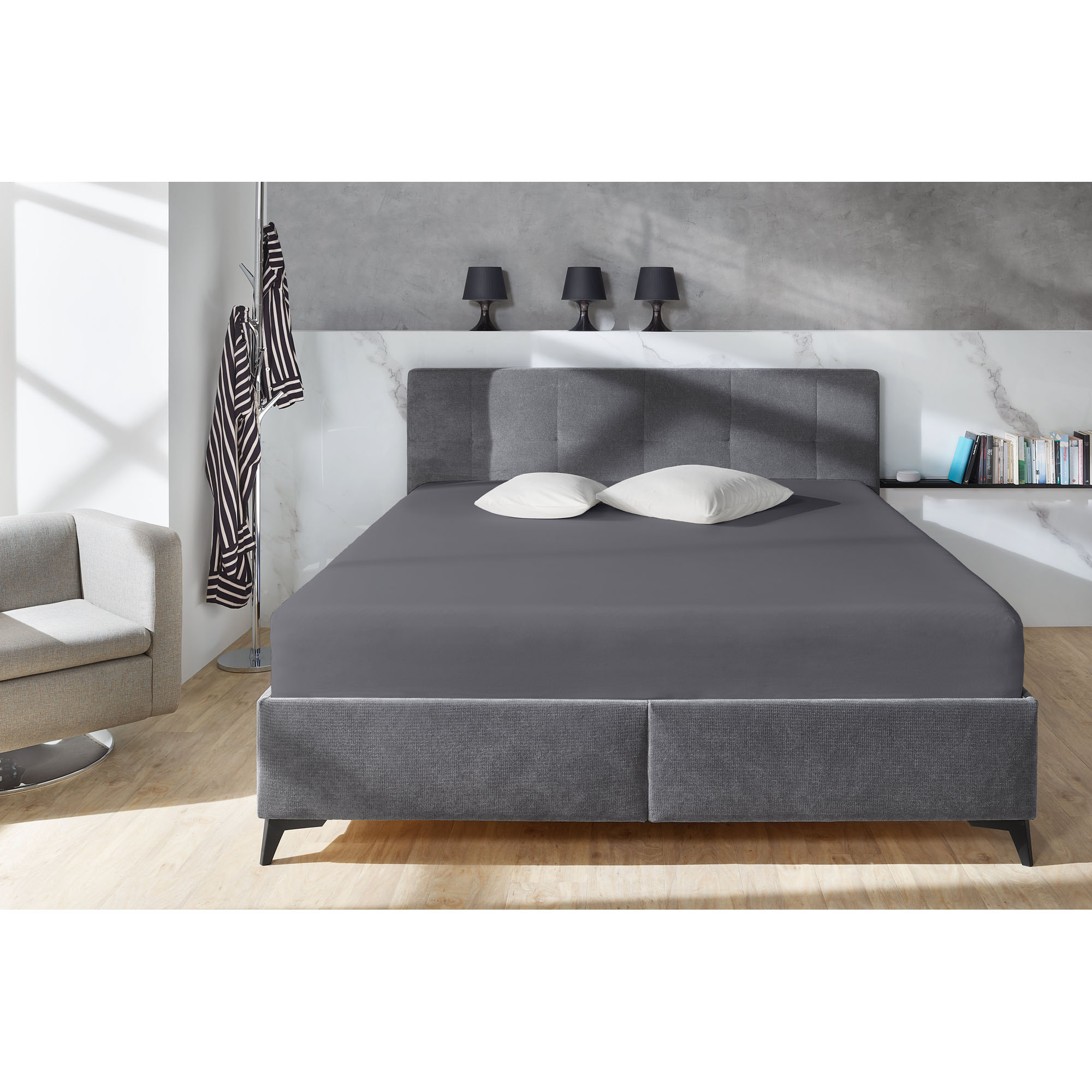 Familien-Spannbetttuch in Anthrazit auf einem grauen Boxspringbett in einem Schlafzimmer; zwei helle Kissen liegen am Kopfende; Größe 240 x 200 cm.