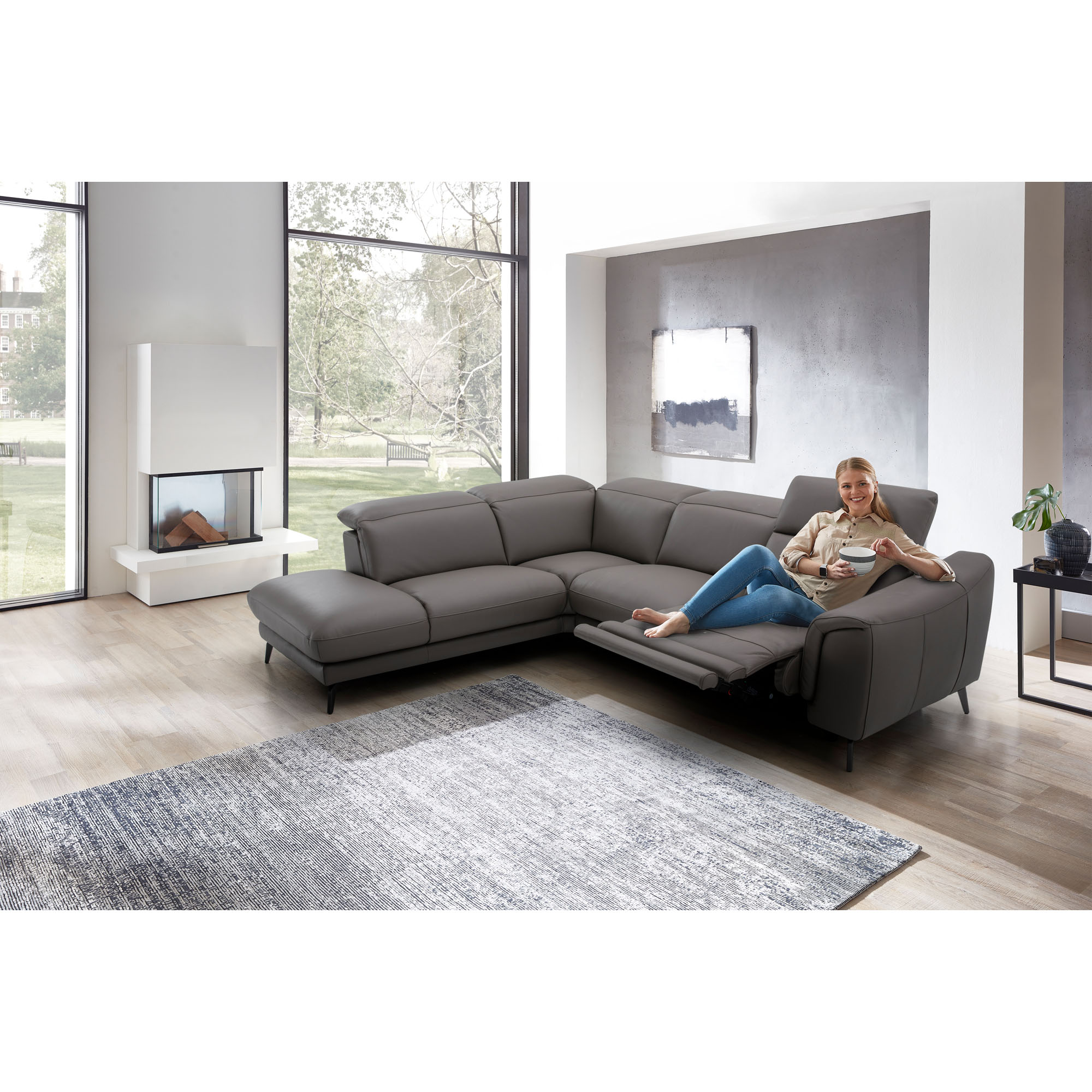 Graues Ecksofa mit Recamiere in einem hellen Wohnraum mit Teppich und großer Fensterfront