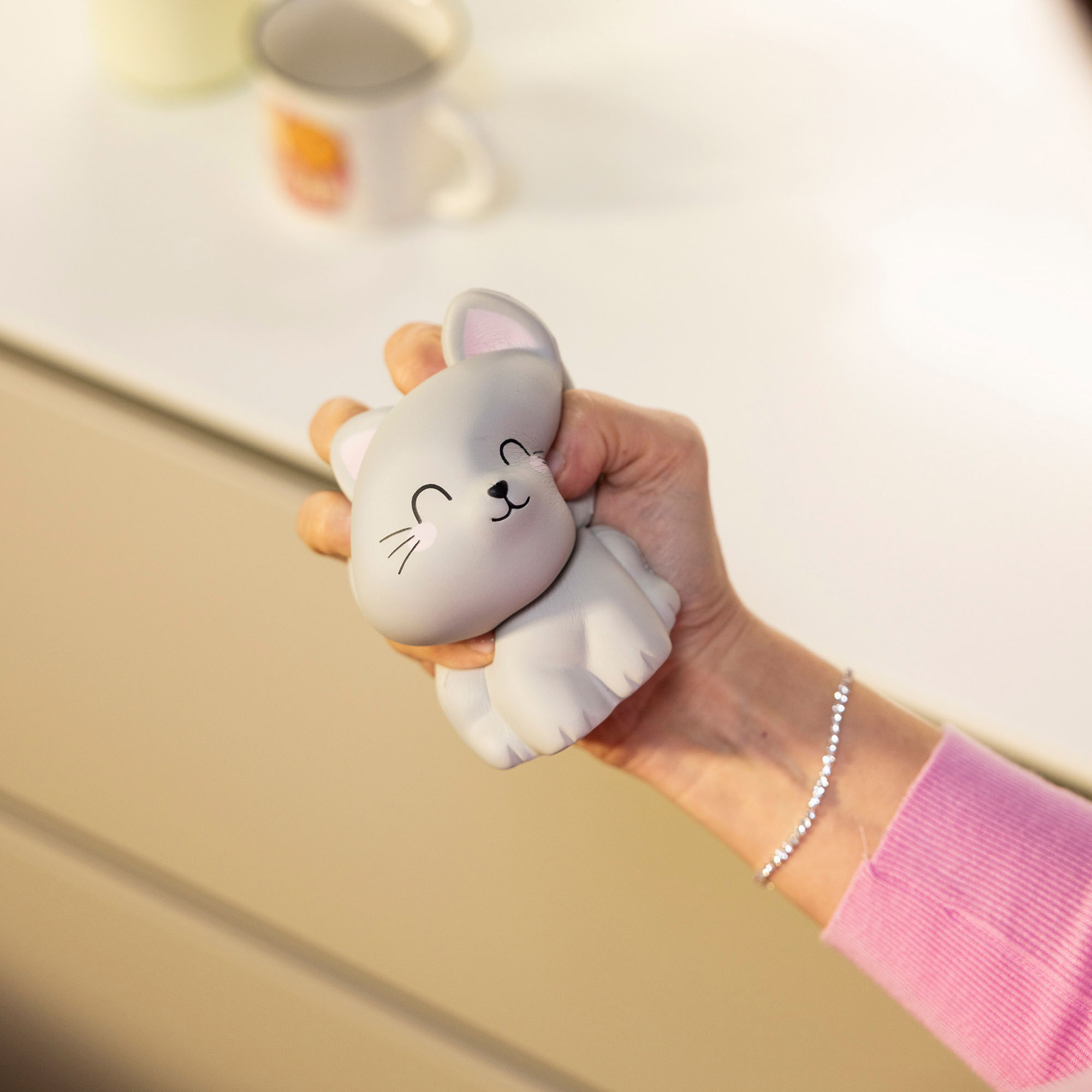 Graue Antistress-Figur in Katzenform, schräg auf einer geöffneten Handfläche dargestellt.