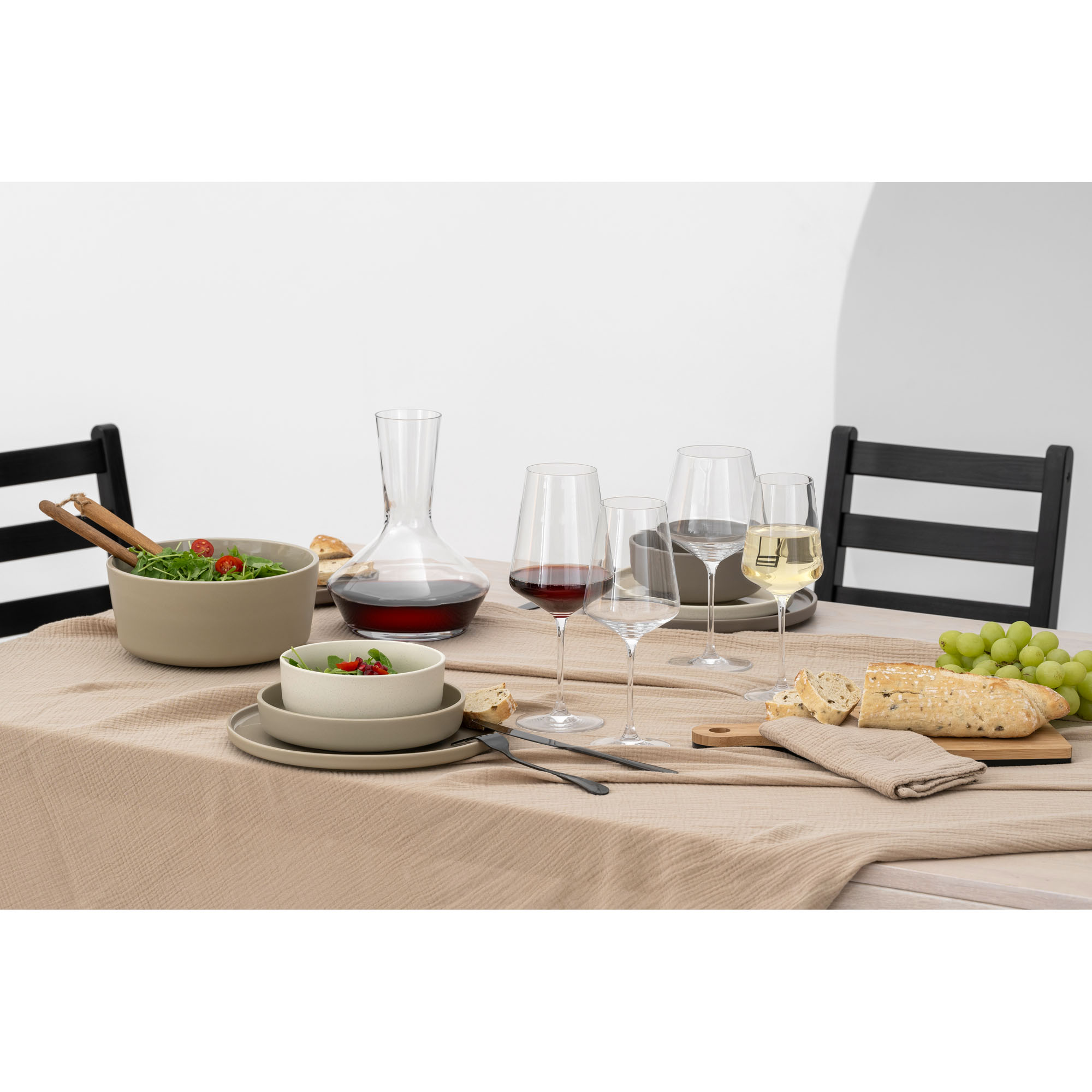 Dekanter mit Rotwein umgeben von Weingläsern und gedecktem Tisch
