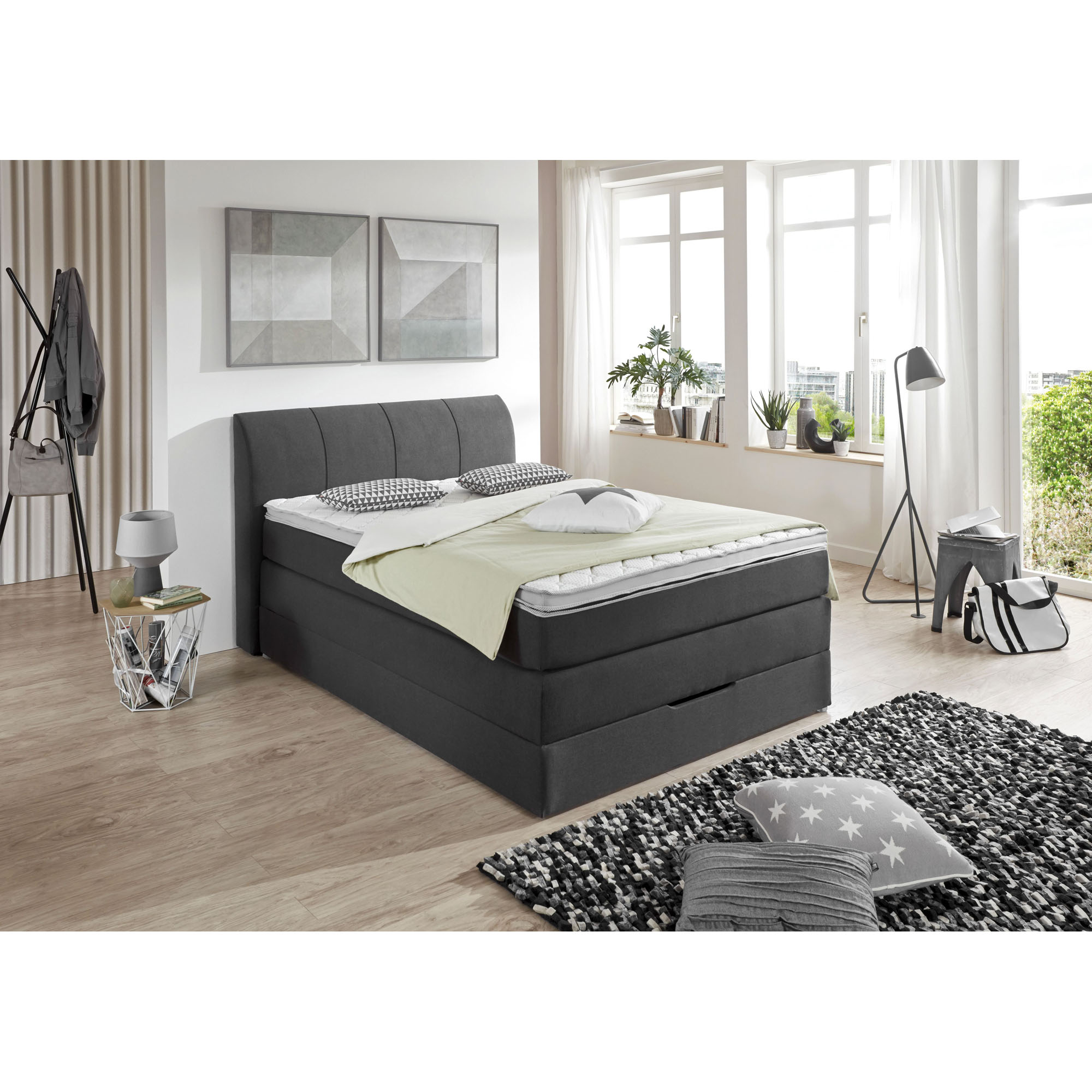Boxspringbett in einem modern eingerichteten Schlafzimmer mit Bildern an der Wand, Stehleuchte und Teppich