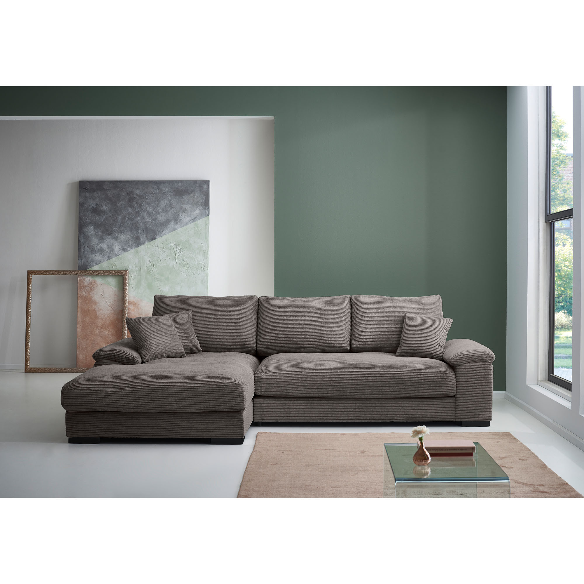 Braune Cord Wohnlandschaft mit Longchair links im Bild, tiefen Sitzflächen, gepolsterten Armlehnen und Zierkissen in einem hellen Wohnzimmer