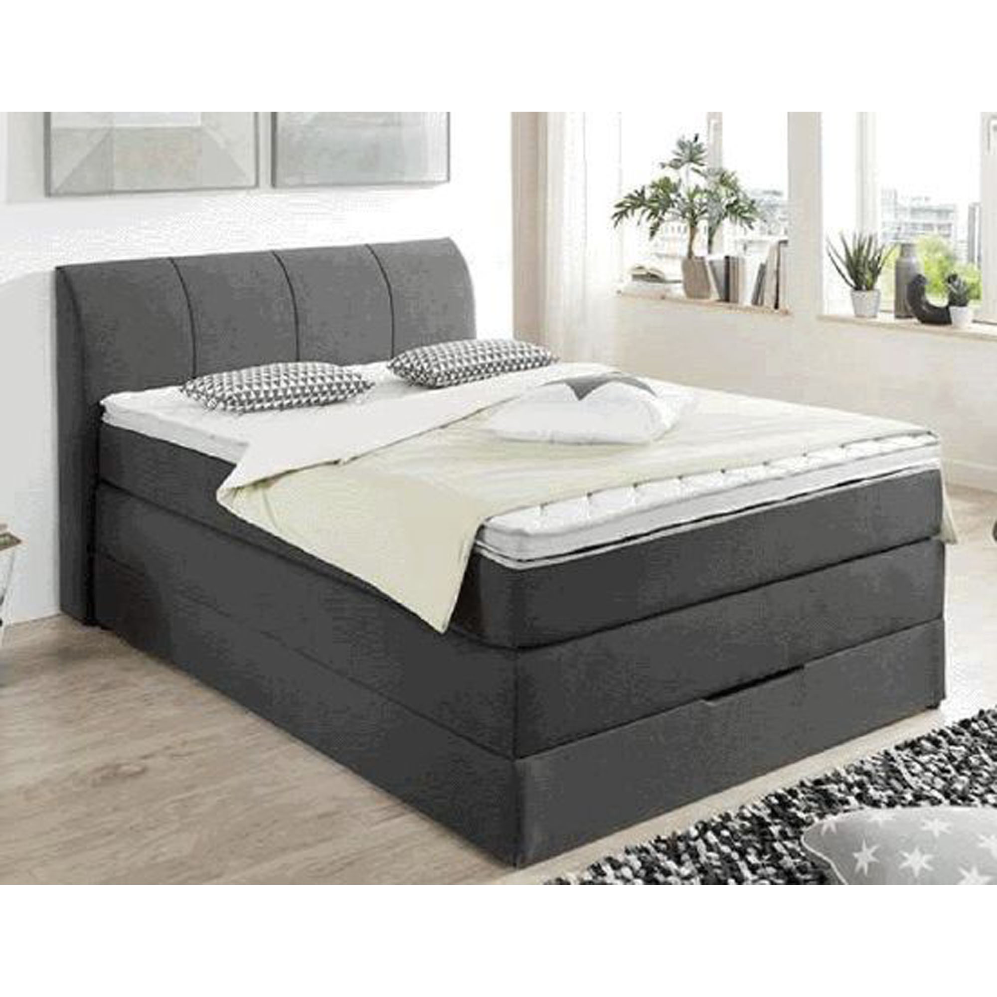 Boxspringbett mit gepolstertem Kopfteil in einem hellen Schlafzimmer mit Fenster, Nachttisch und Teppich