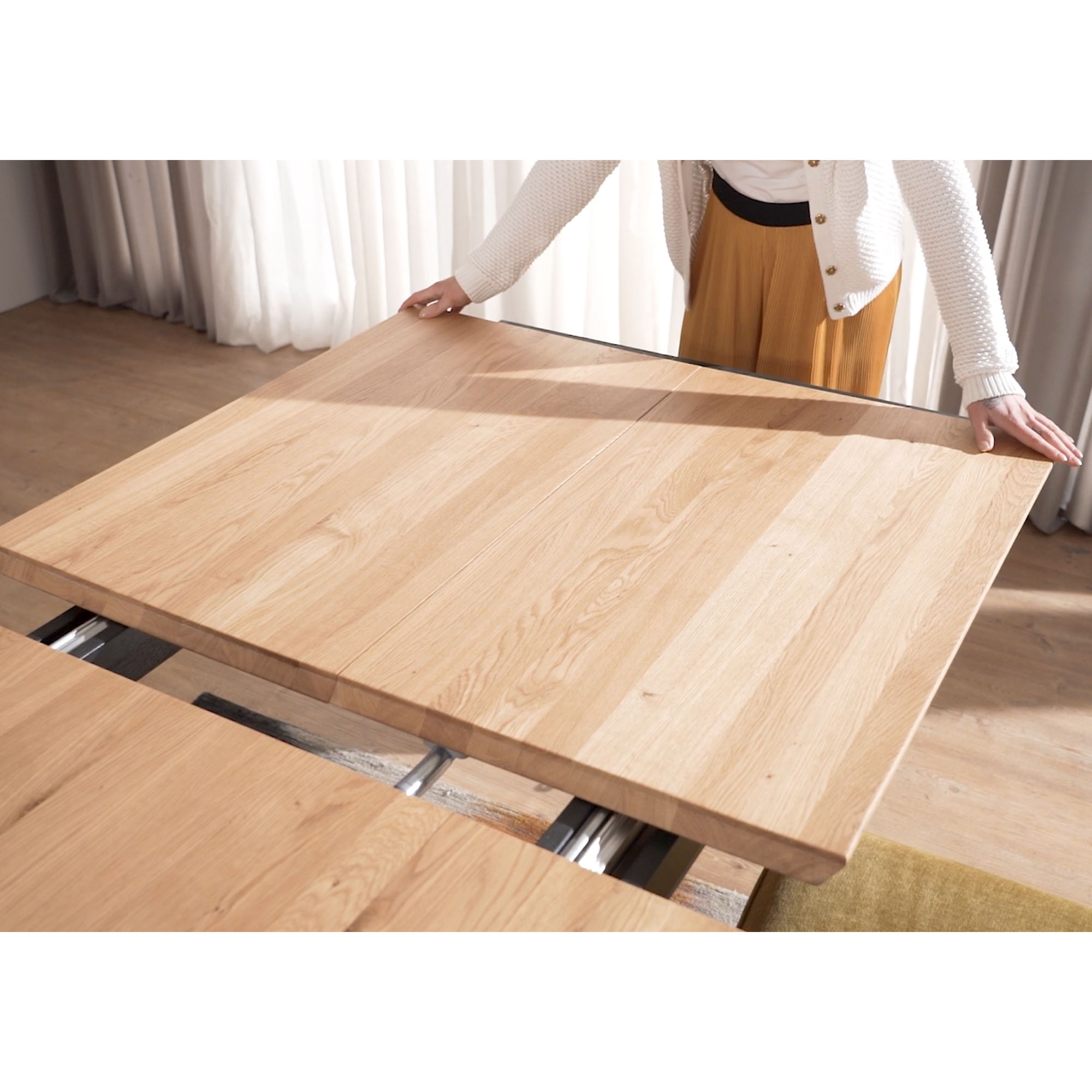 Person legt die Erweiterungsplatten eines ausziehbaren Esstisches mit Holzplatte ein