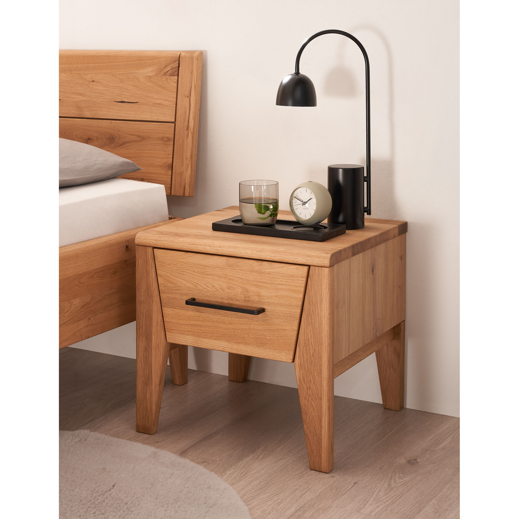 Nachttisch aus Holz mit Schublade aus seitlicher Perspektive neben einem Bett