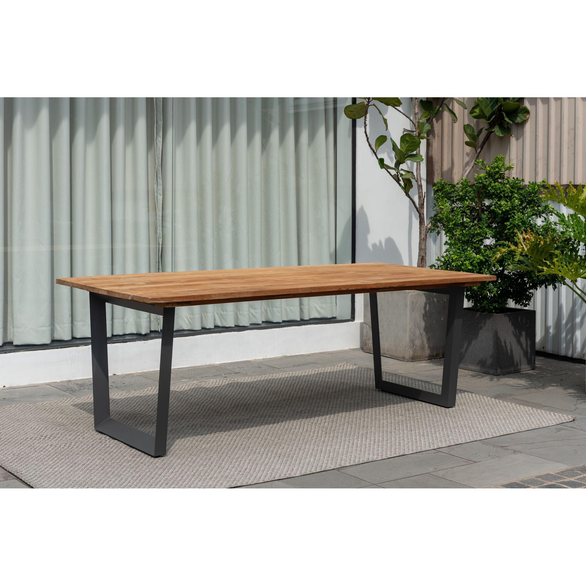 Langer Gartentisch aus Holz mit schwarzem Metallgestell, auf Terrasse mit Pflanzen und Teppich dekorativ platziert.