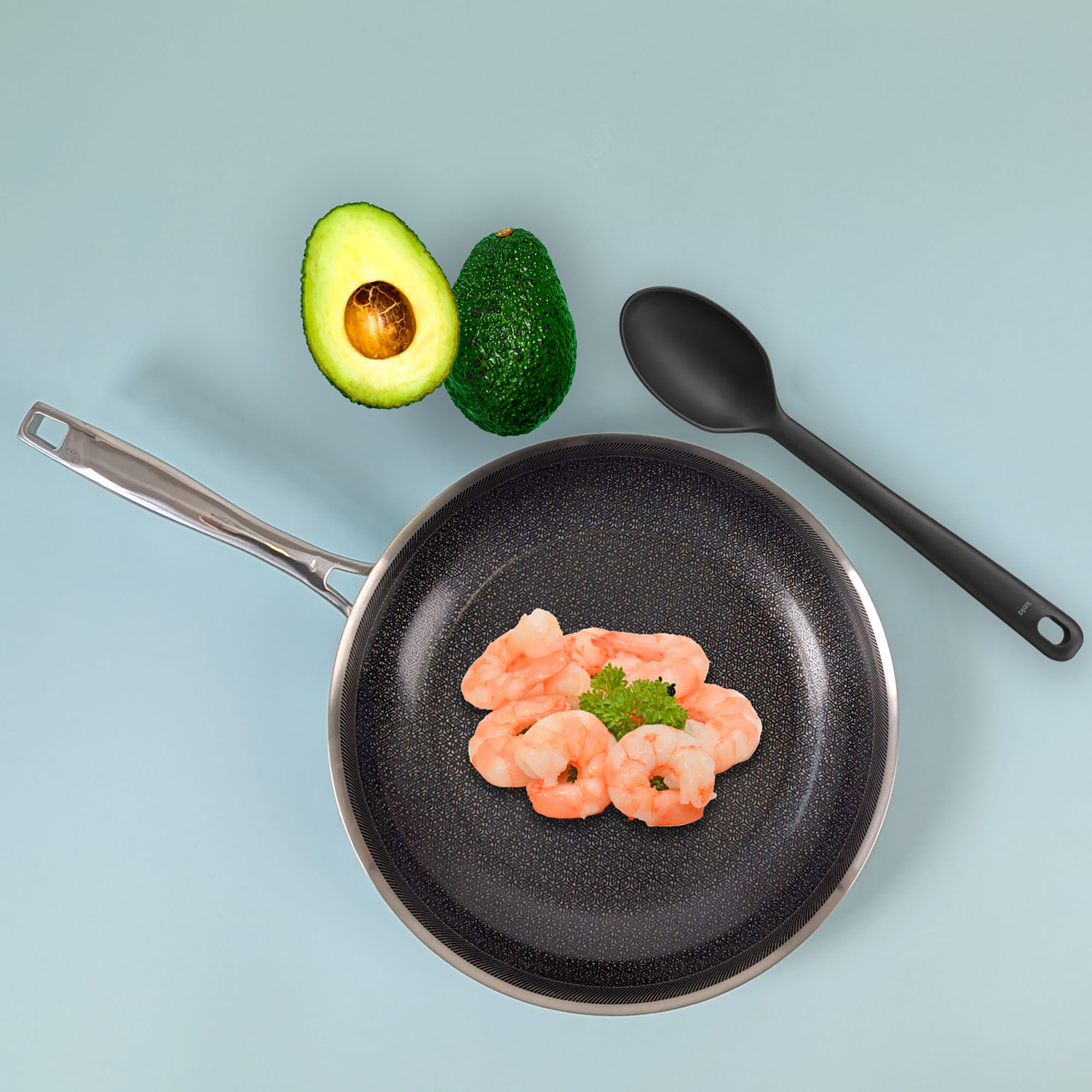 Bratpfanne mit Garnelen auf einer Kochfläche neben einer halbierten Avocado