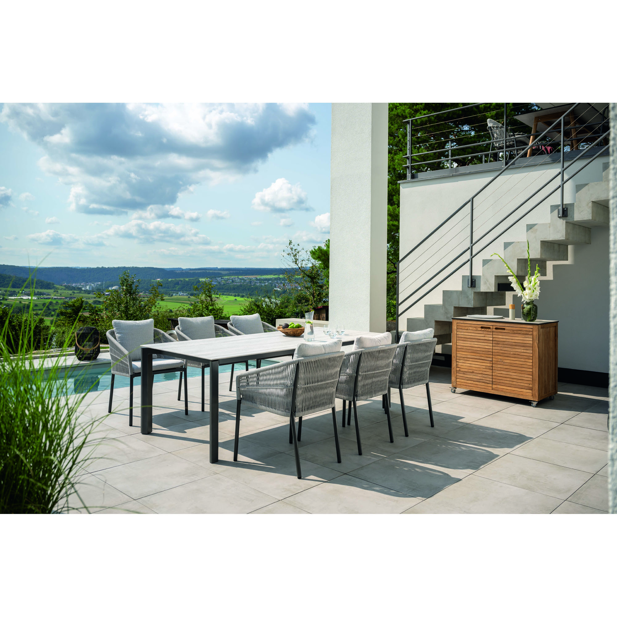 Ein Gartentisch mit Tischplatte und mehreren Stühlen auf einer Terrasse, mit weitem Landschaftsblick im Hintergrund.