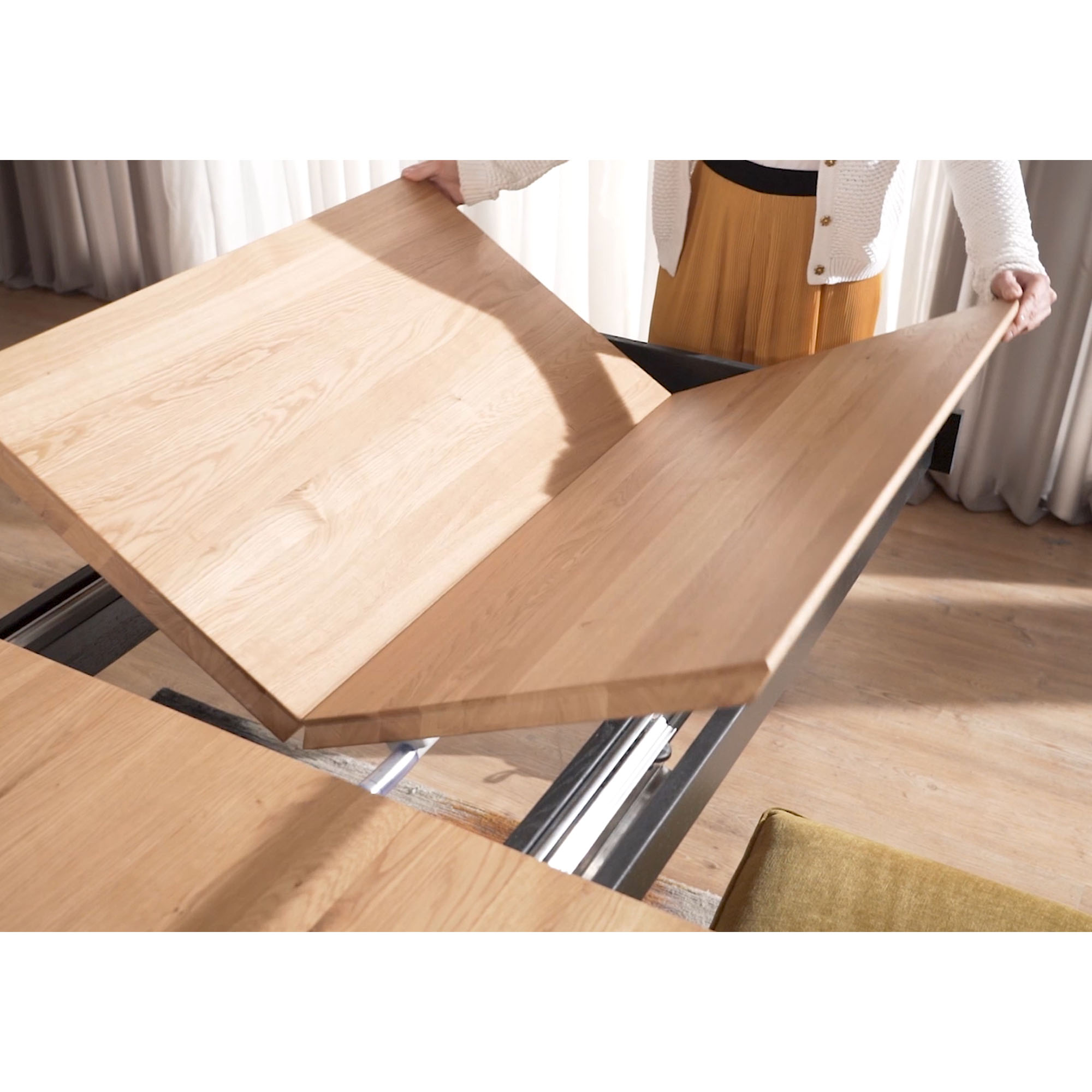 Person hebt die mittleren Erweiterungsplatten eines ausziehbaren Esstisches mit Holzplatte an