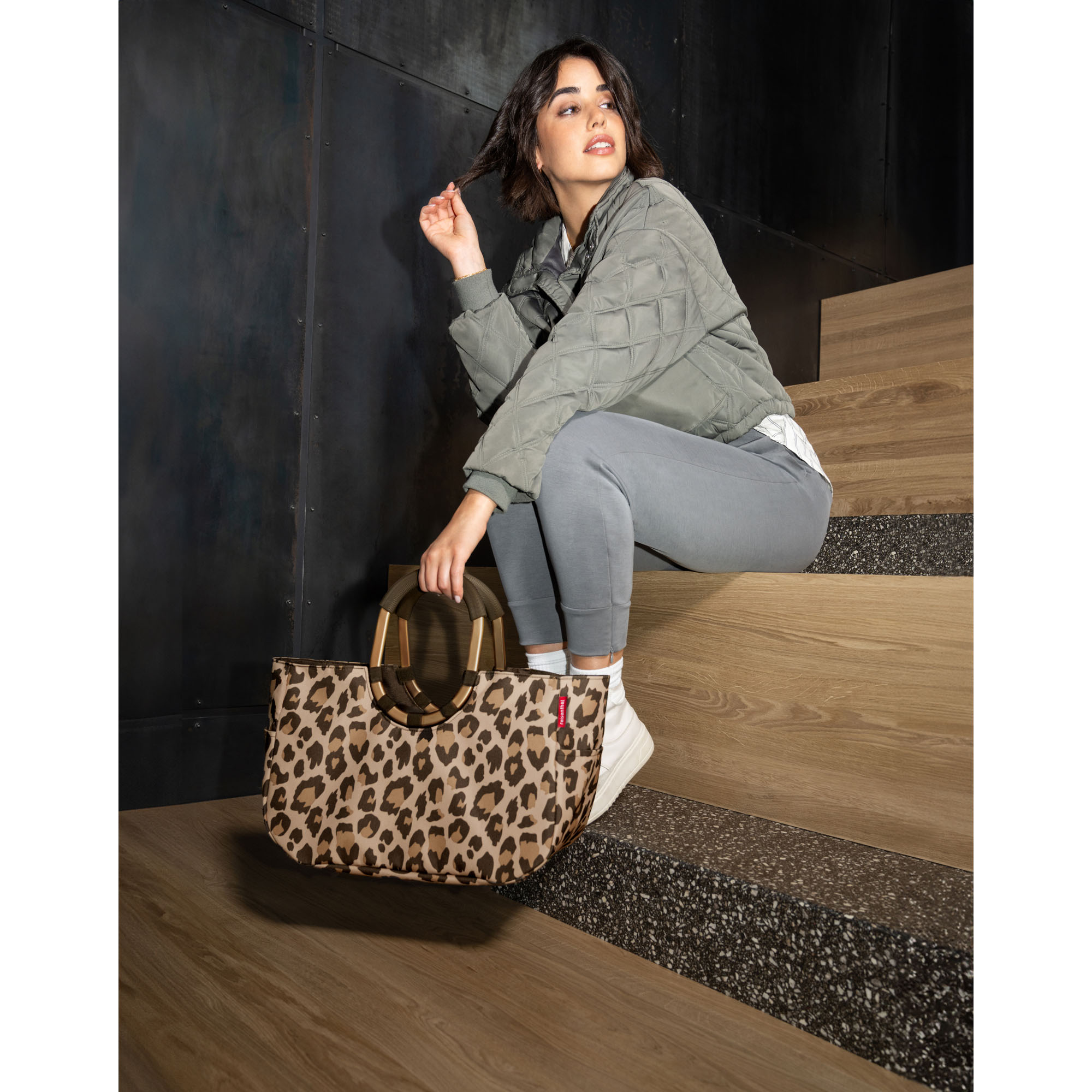 Shopper von Reisenthel, Modell Loopshopper M, in Beige und Braun mit Leopardenmuster und braun-goldfarbenen Rahmendetails, von einer Person an einem Ringgriff getragen.