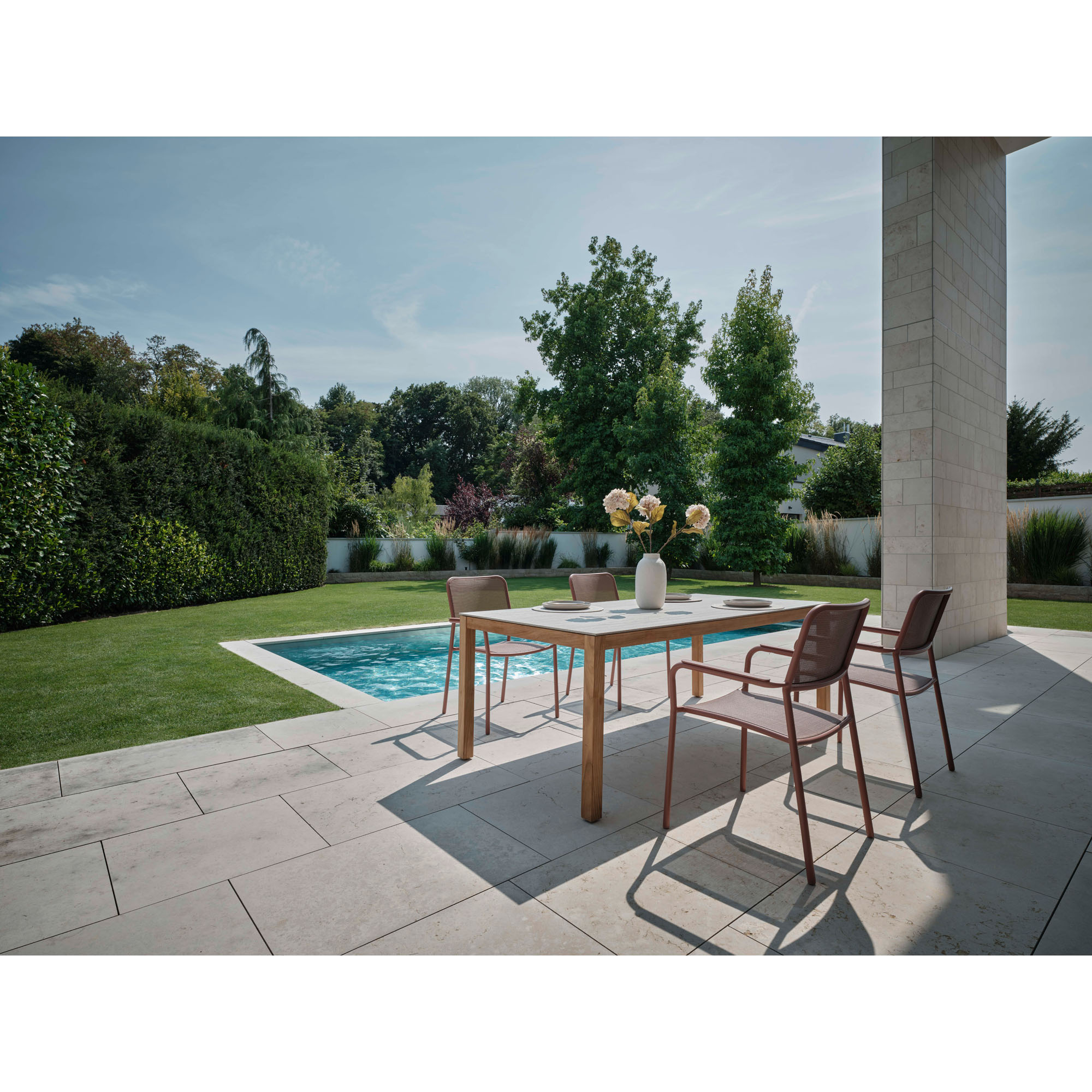 Mehrere Gartenstühle mit Armlehnen an einem rechteckigen Tisch auf einer Terrasse neben einem Pool