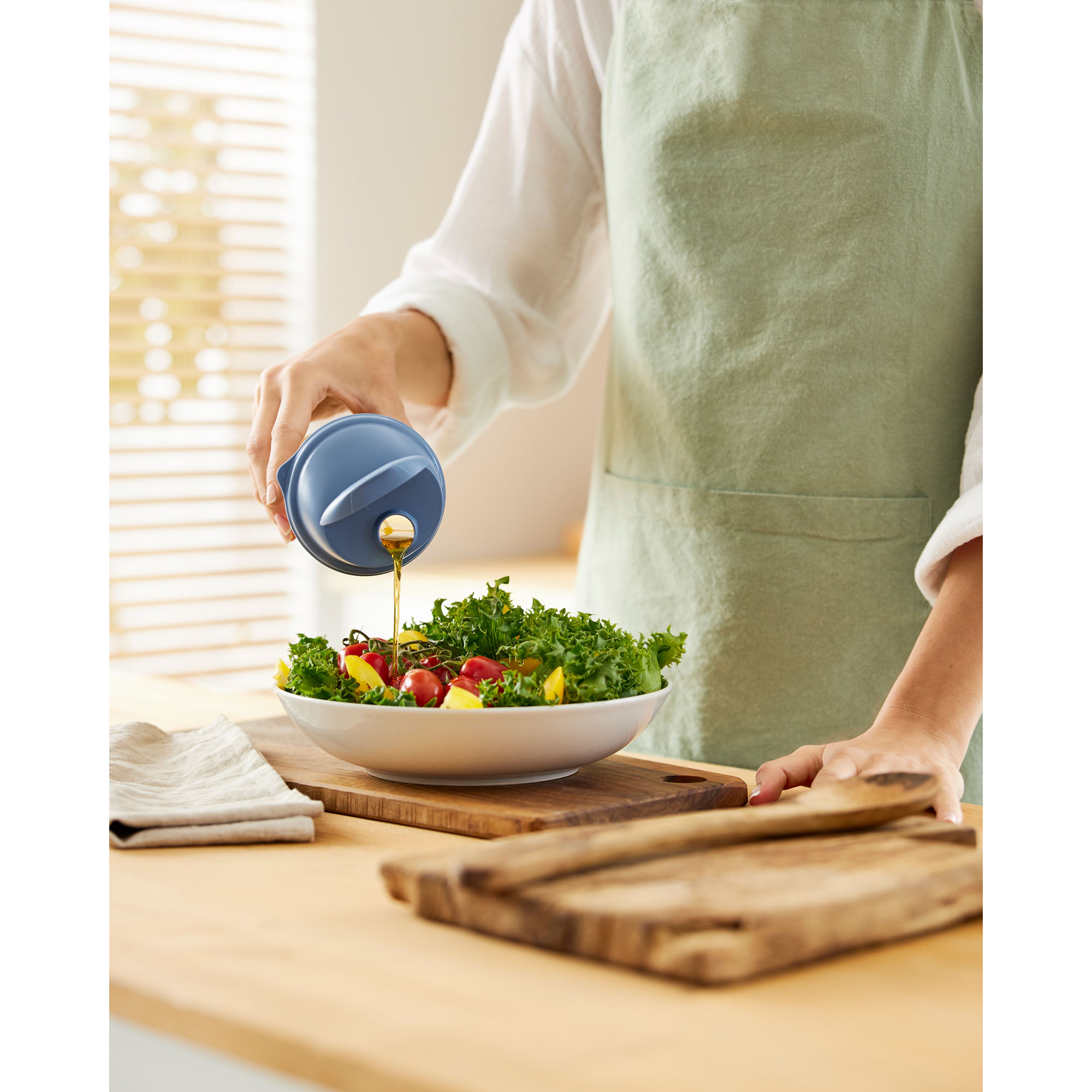 Transparenter Shaker mit blauem Deckel wird zum Ausgießen über einer Salatschüssel verwendet