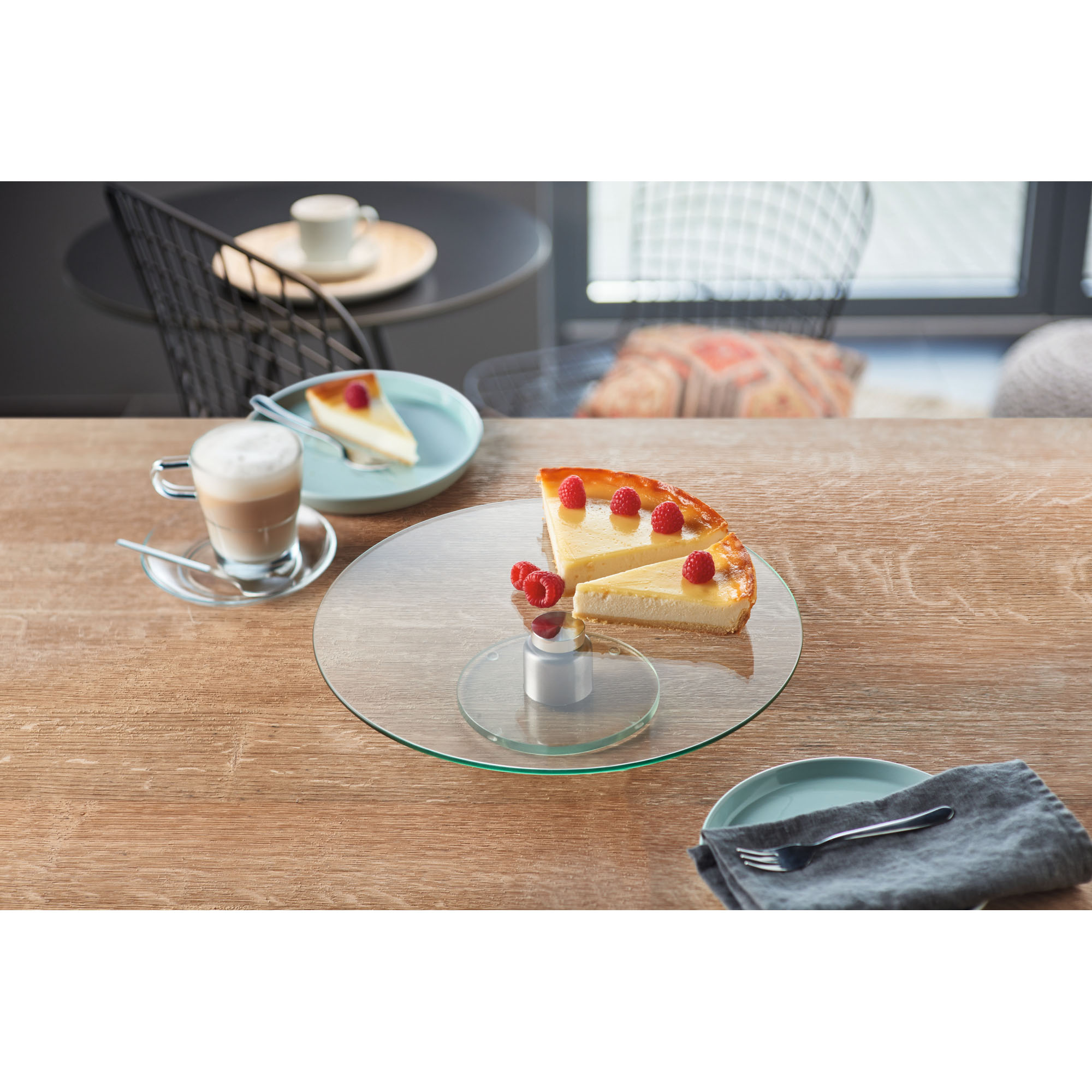 Runde Glas-Tortenplatte auf Tisch mit Kuchenstück und gedeckter Kaffeetafel