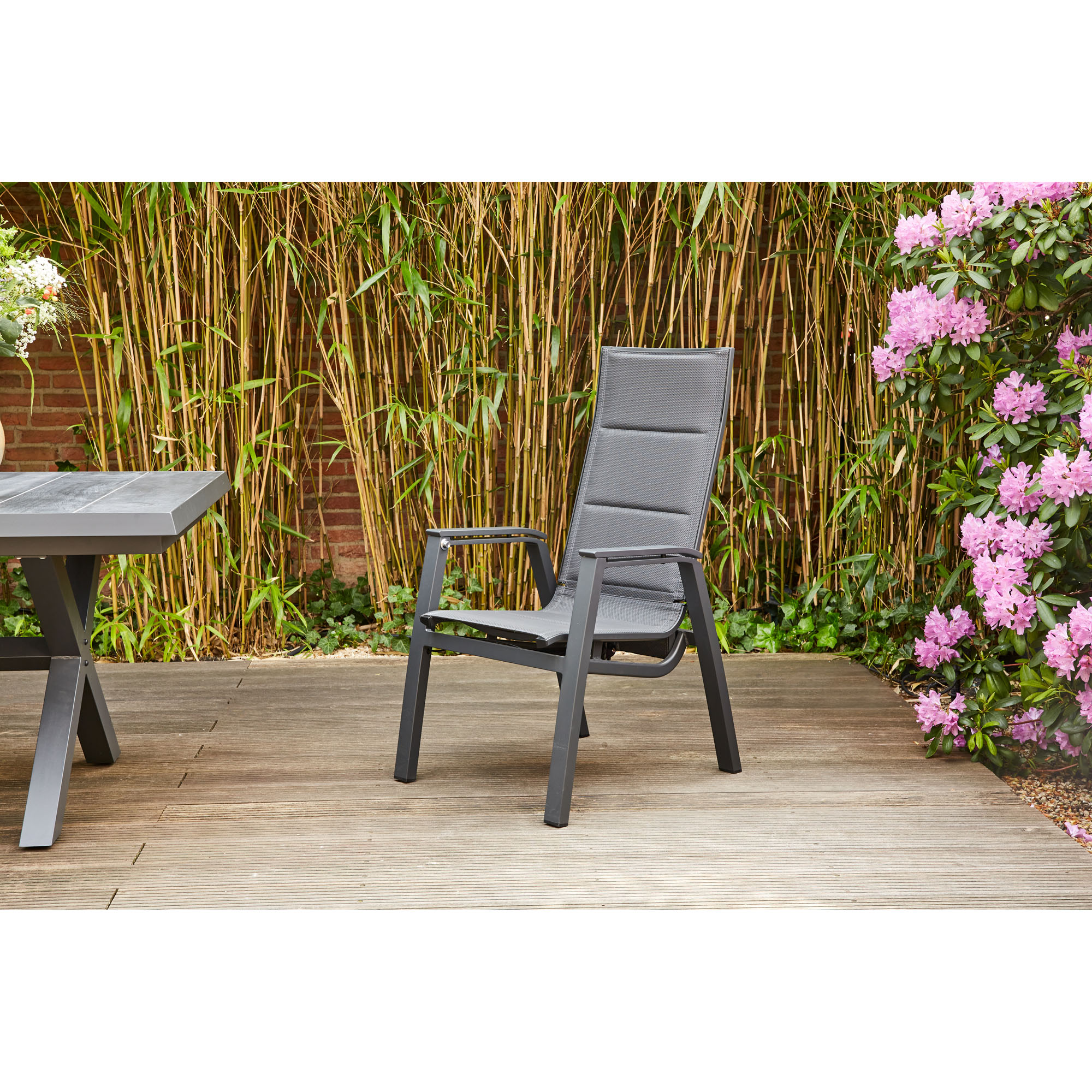 Schwarzer verstellbarer Gartenstuhl aus Aluminium mit hoher Rückenlehne auf einer Terrasse neben Tisch und Pflanzen