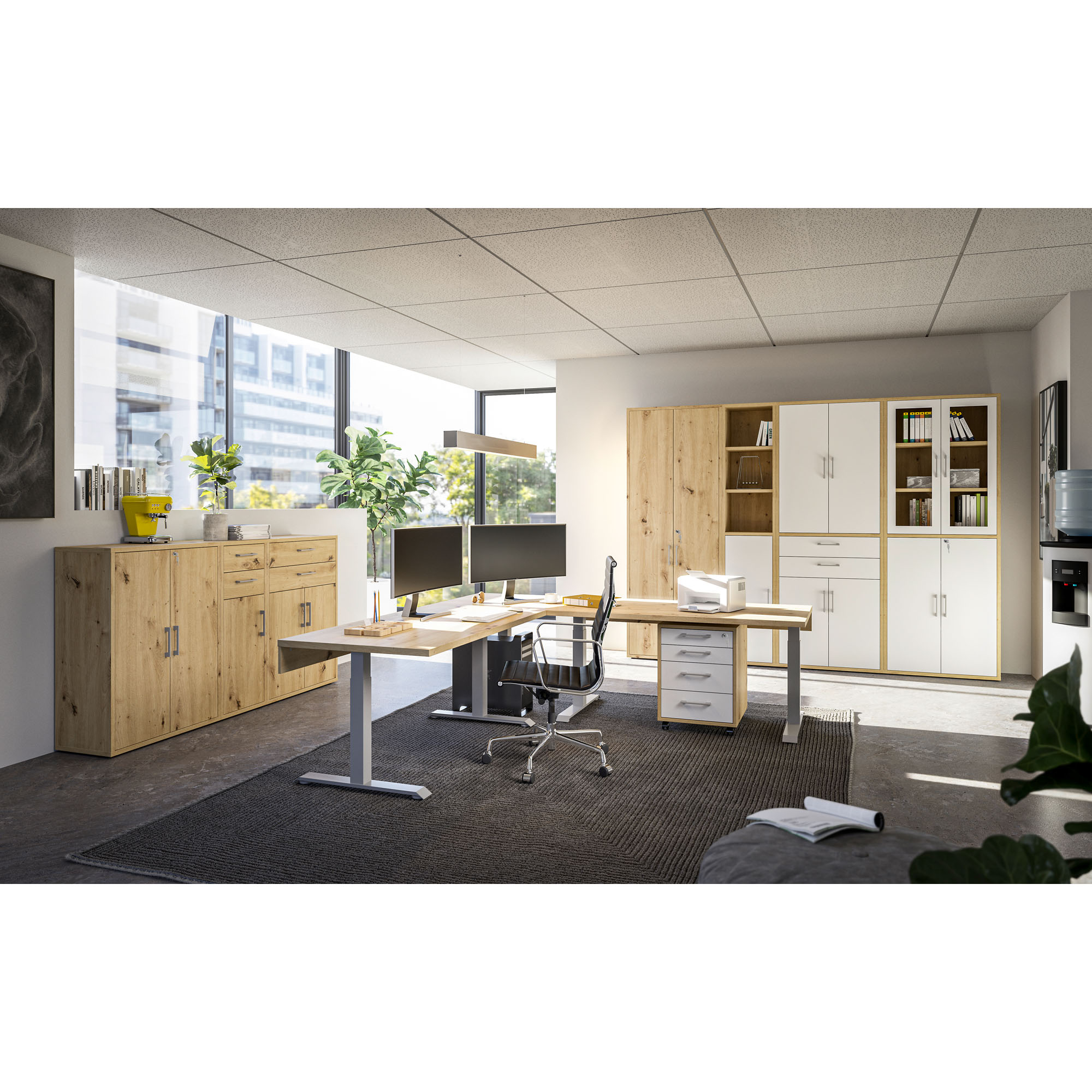 elles Büro mit Schreibtisch, Rollcontainer, Regalen und Schränken in Holz und Weiß, zwei Monitore auf dem Schreibtisch, große Fenster mit Pflanzen im Hintergrund