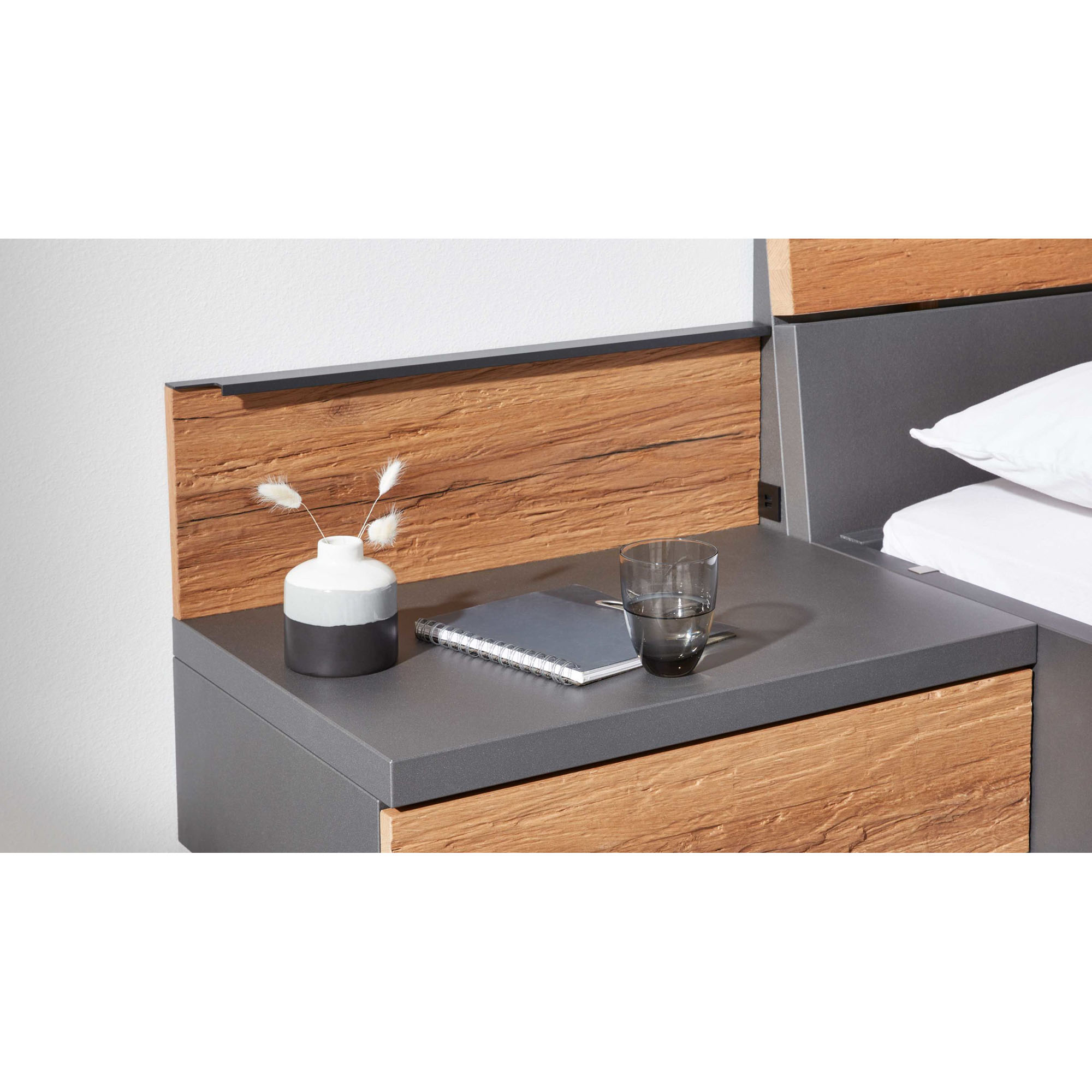 Interliving 1025 Aufsatzpaneel in Holzoptik über einem Nachttisch neben einem Bett montiert