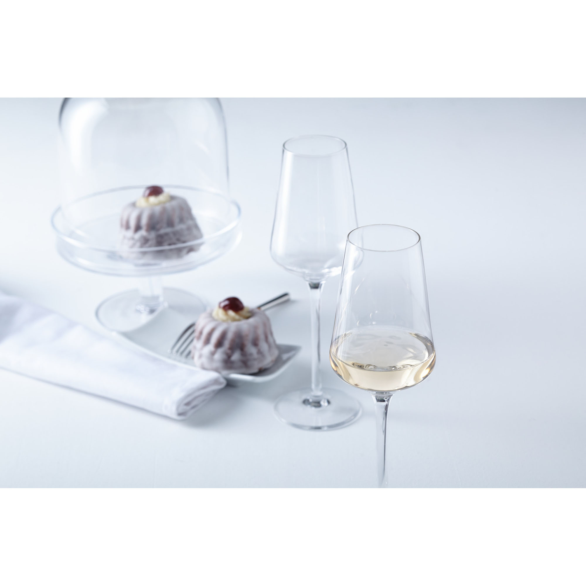 Zwei Weißweingläser neben kleinen Desserts auf hellem Tisch