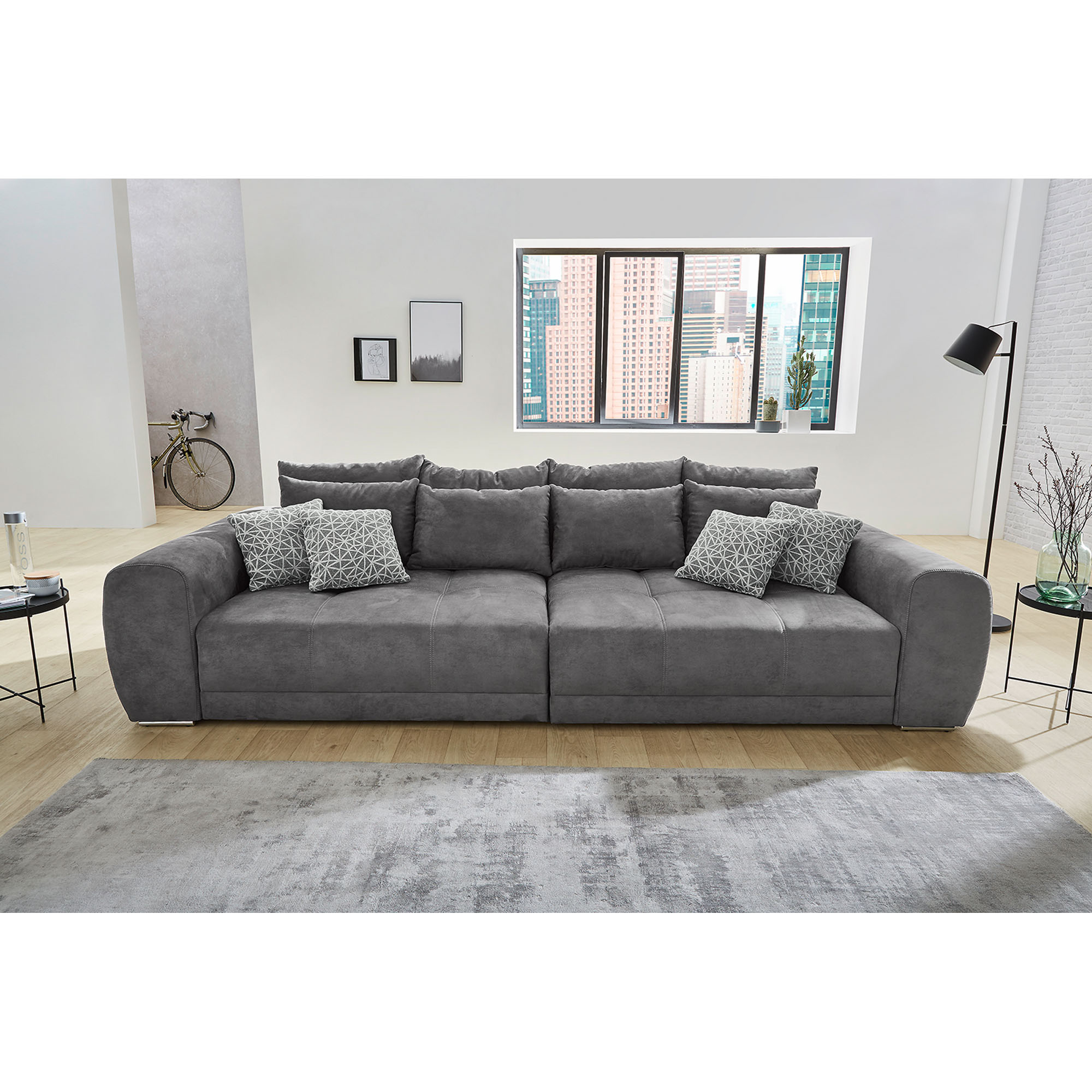 Bigsofa in Grau, Stellmaß 134x306 cm, mit großen Kissen in Dunkelgrau und kleinen Kissen in Hellgrau, dargestellt in einem Wohnzimmer