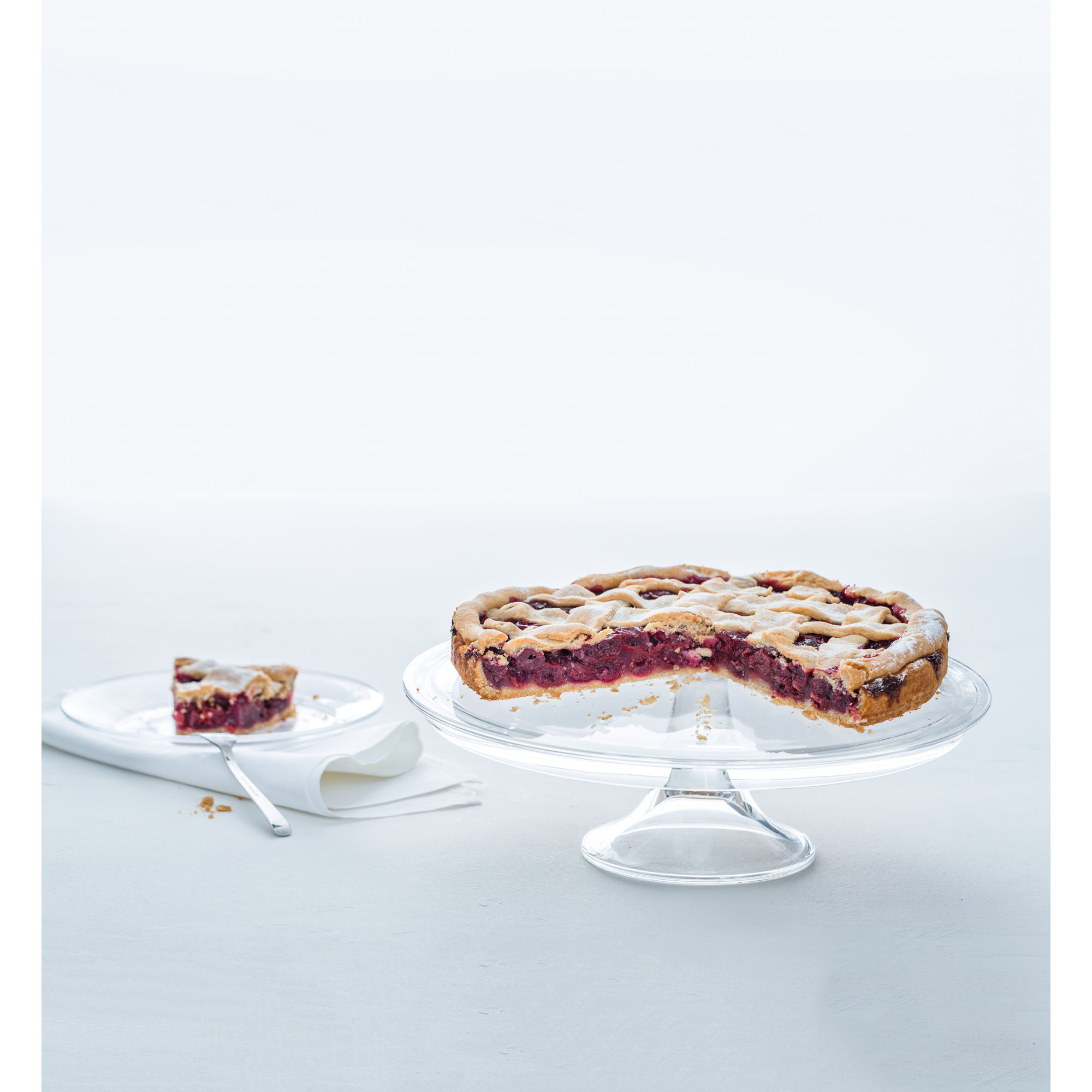 Glas Tortenplatte mit angeschnittenem Kuchen auf hellem Hintergrund