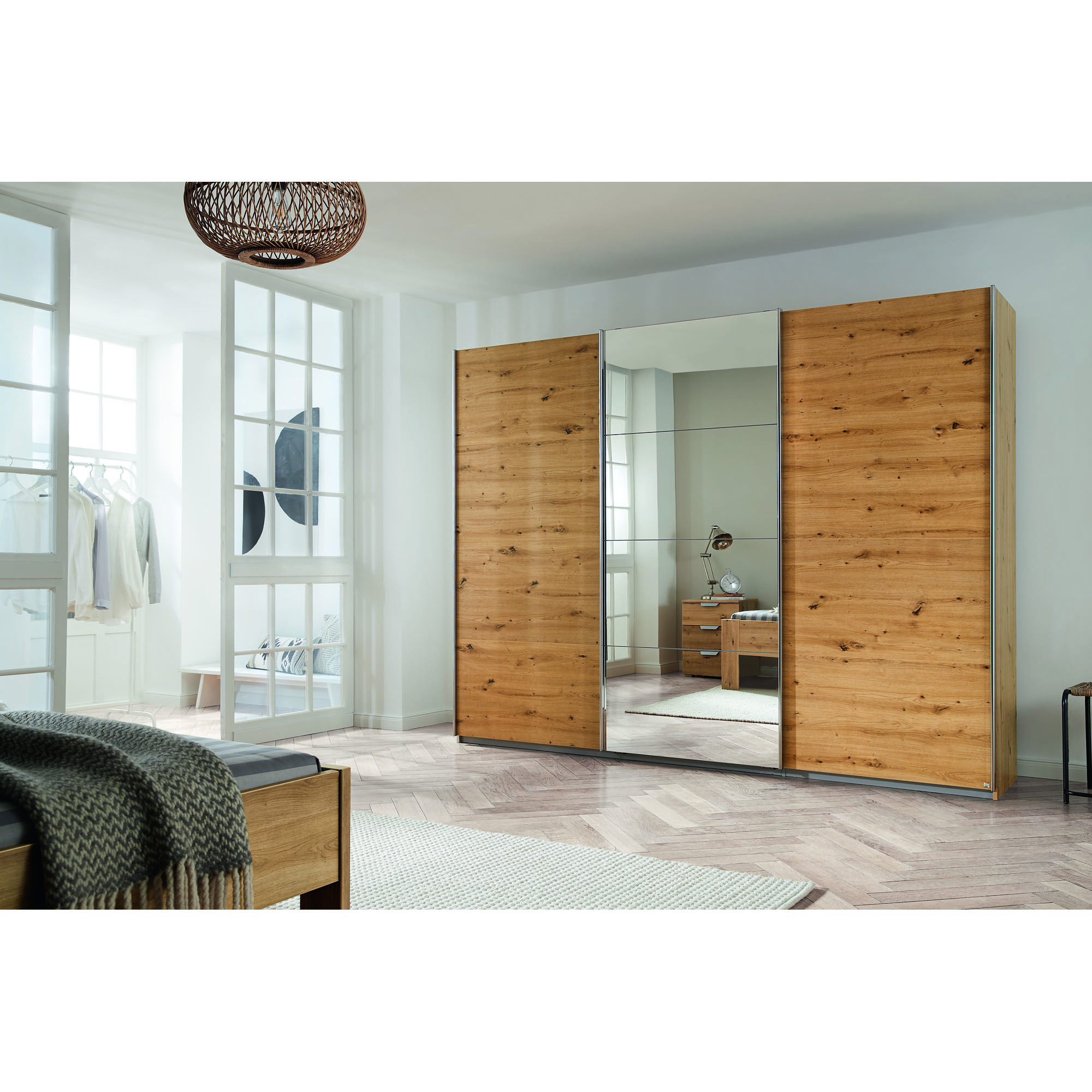 Schwebetürenschrank mit drei Türen, Korpus in Dekor Artisan Eiche und Front in Alu-Optik, mittlere Tür als Spiegelfront, aufgestellt in einem Schlafzimmer.