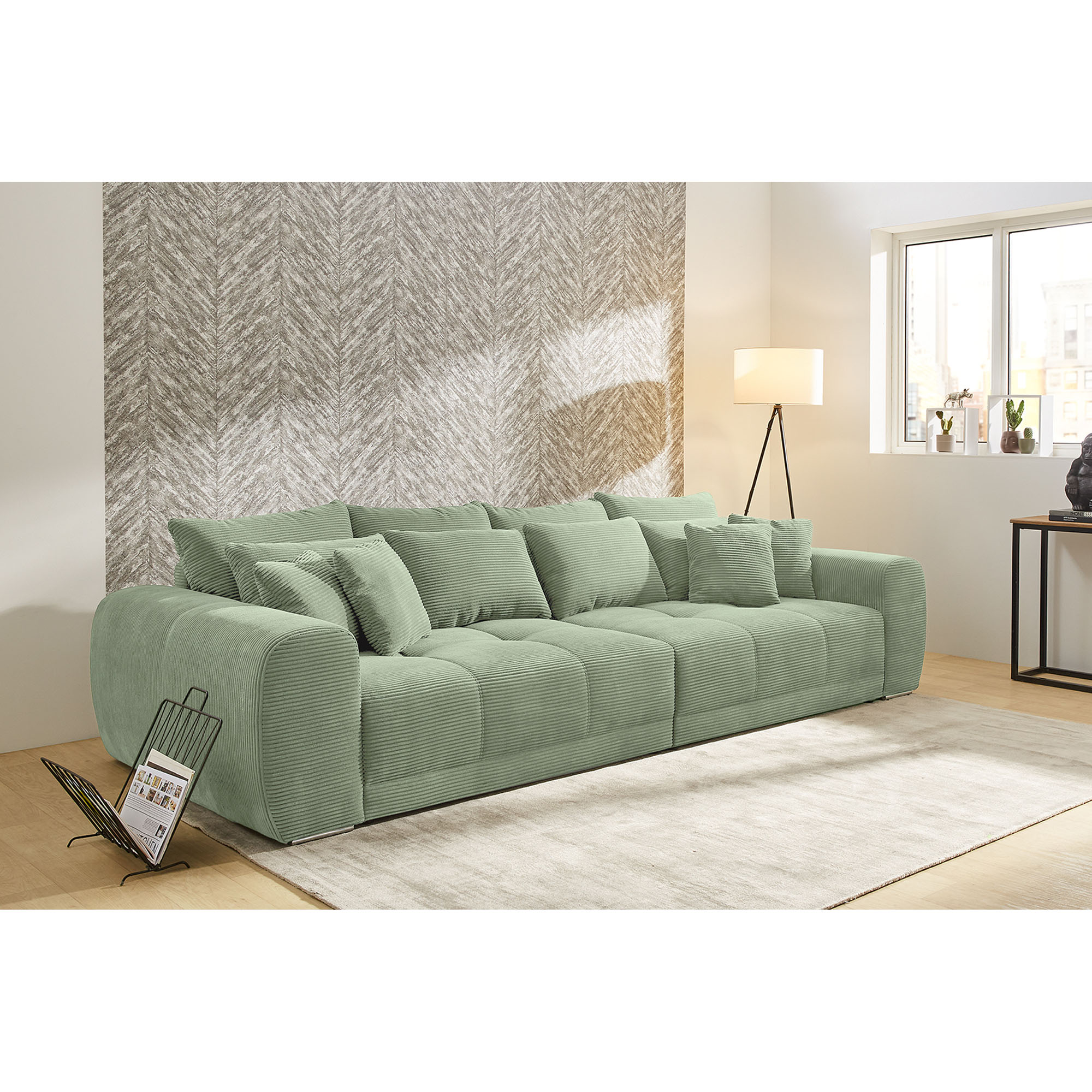 Großes grünes Cordsofa mit vielen Kissen in modern eingerichteter Wohnlandschaft mit Teppich und Stehlampe