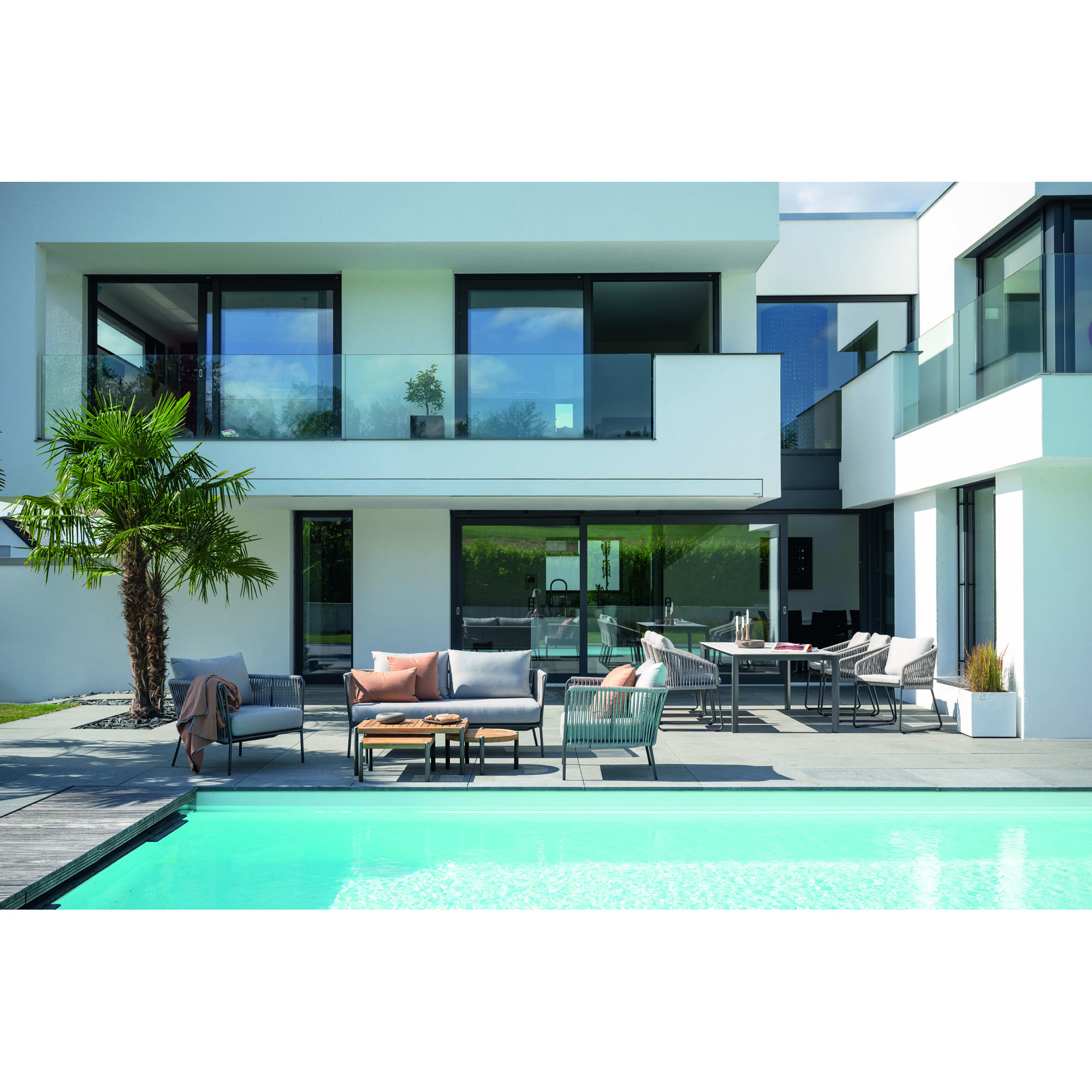Gartensitzgruppe mit Tisch und Sitzmöbeln auf einer Terrasse vor einem modernen Wohnhaus mit Pool