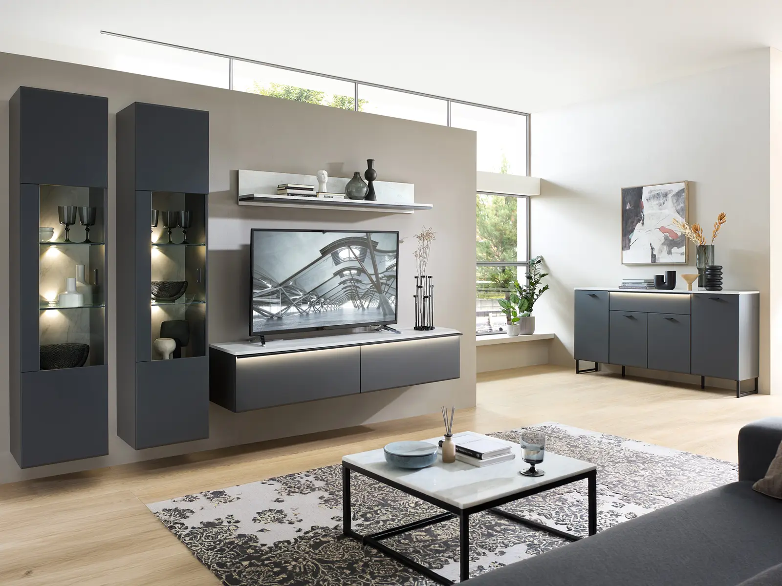 Wohnzimmer mit schwarzem Wohnprogramm Tibor, zwei beleuchteten Vitrinen, TV Lowboard, Wandboard, Sideboard und Couchtisch im Raum