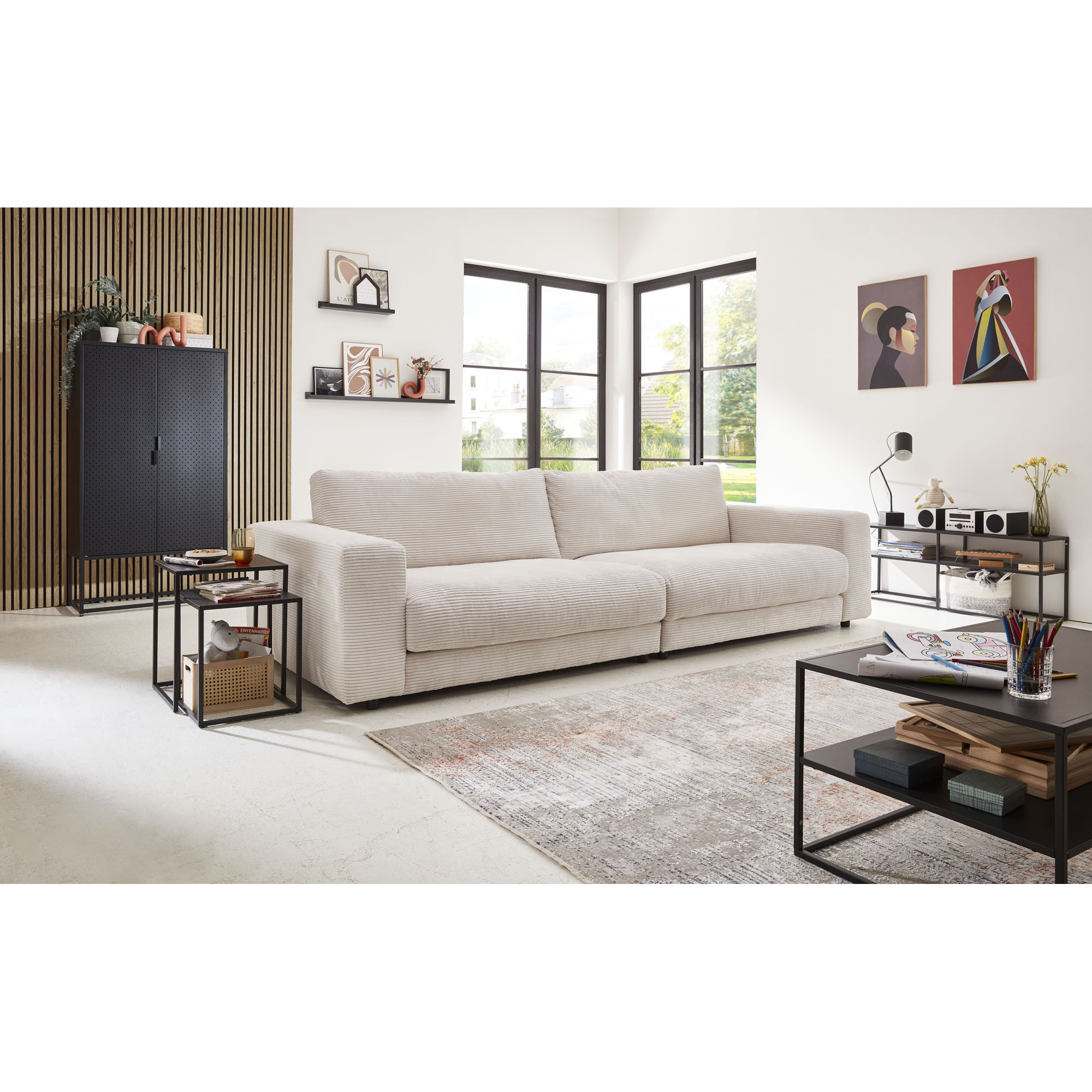 Großes Sofa mit breiten Armlehnen in einem hellen Wohnraum mit Beistelltischen und Teppich