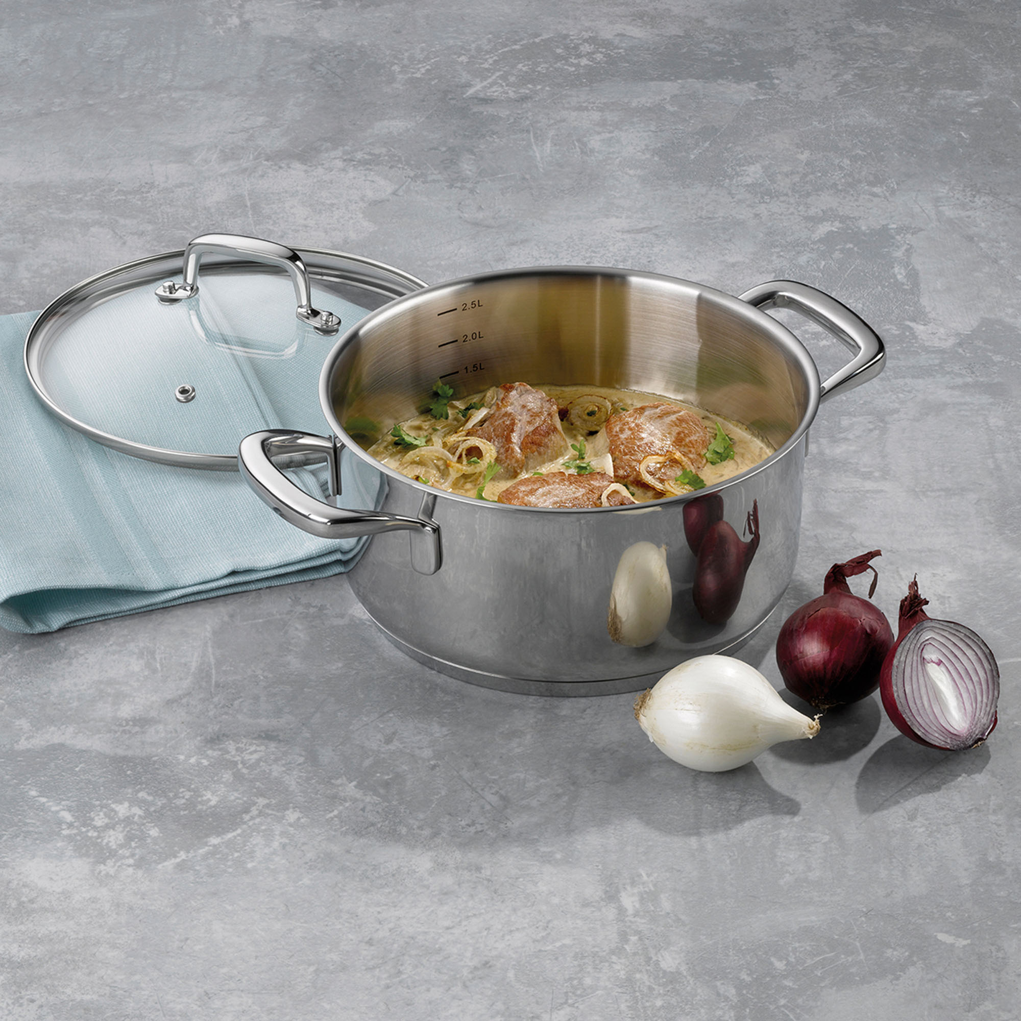 Geöffneter silberfarbener Bratentopf mit einem zubereiteten Gericht neben Glasdeckel, Knoblauch und roten Zwiebeln
